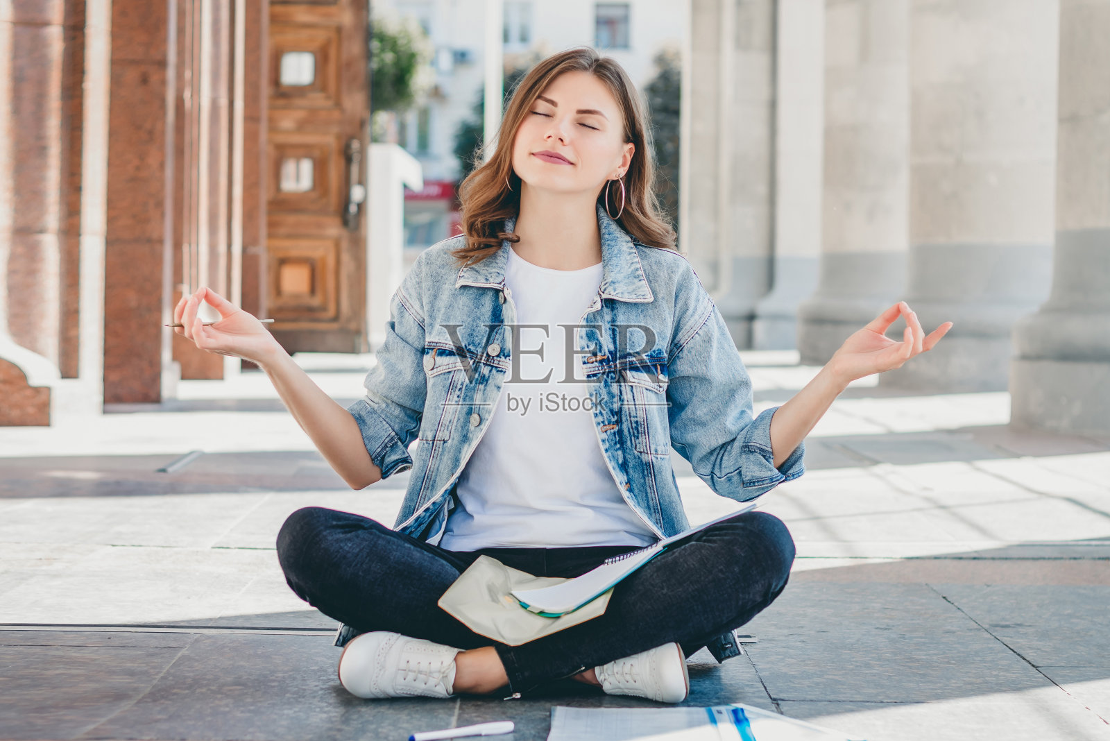 女学生坐在地板上冥想。可爱的女孩要求在考试中取得好成绩。女孩以莲花姿势祈祷。照片摄影图片