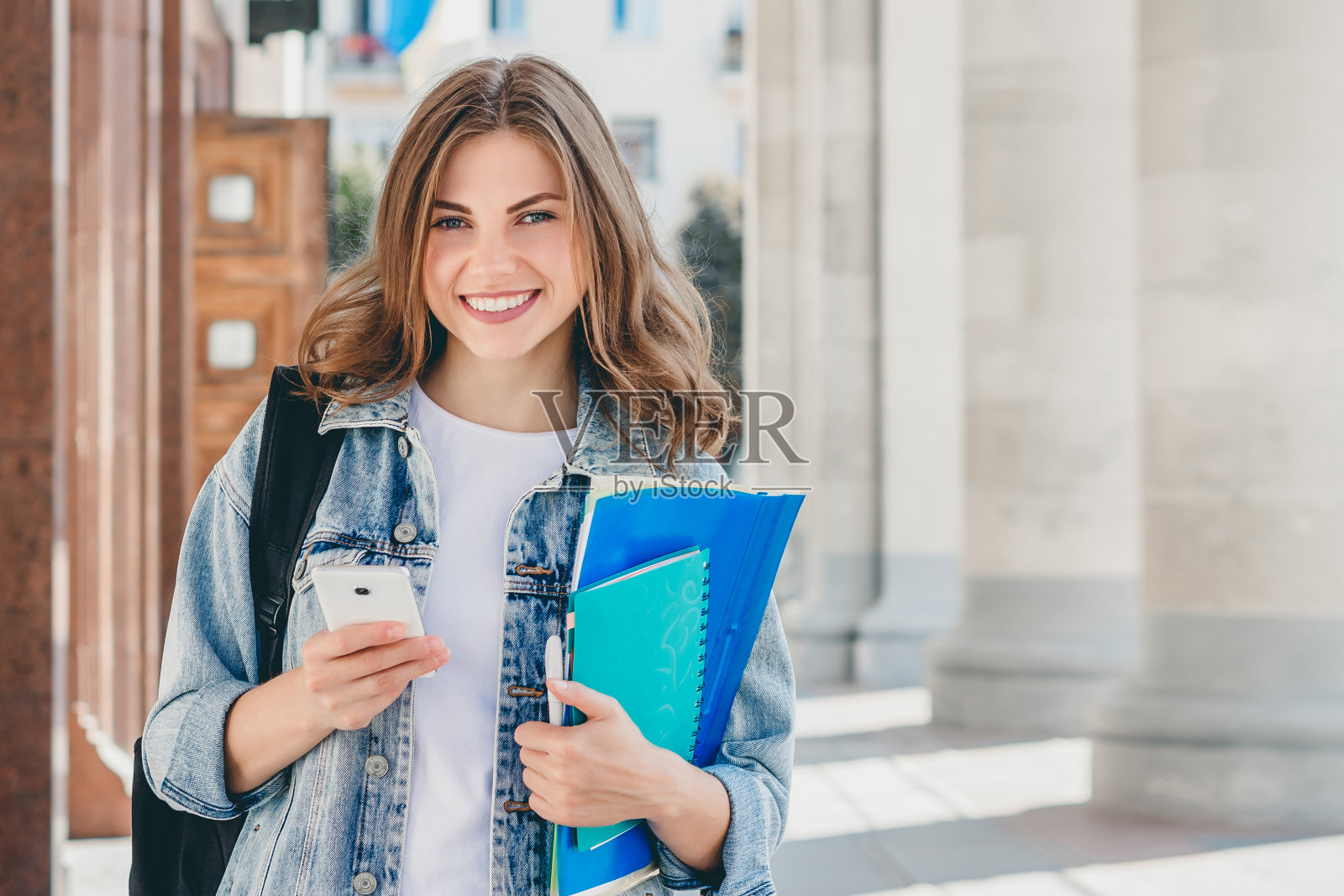 年轻的女学生对着大学微笑。可爱的女学生手里拿着文件夹、笔记本和手机。学习、教育理念与拷贝空间照片摄影图片