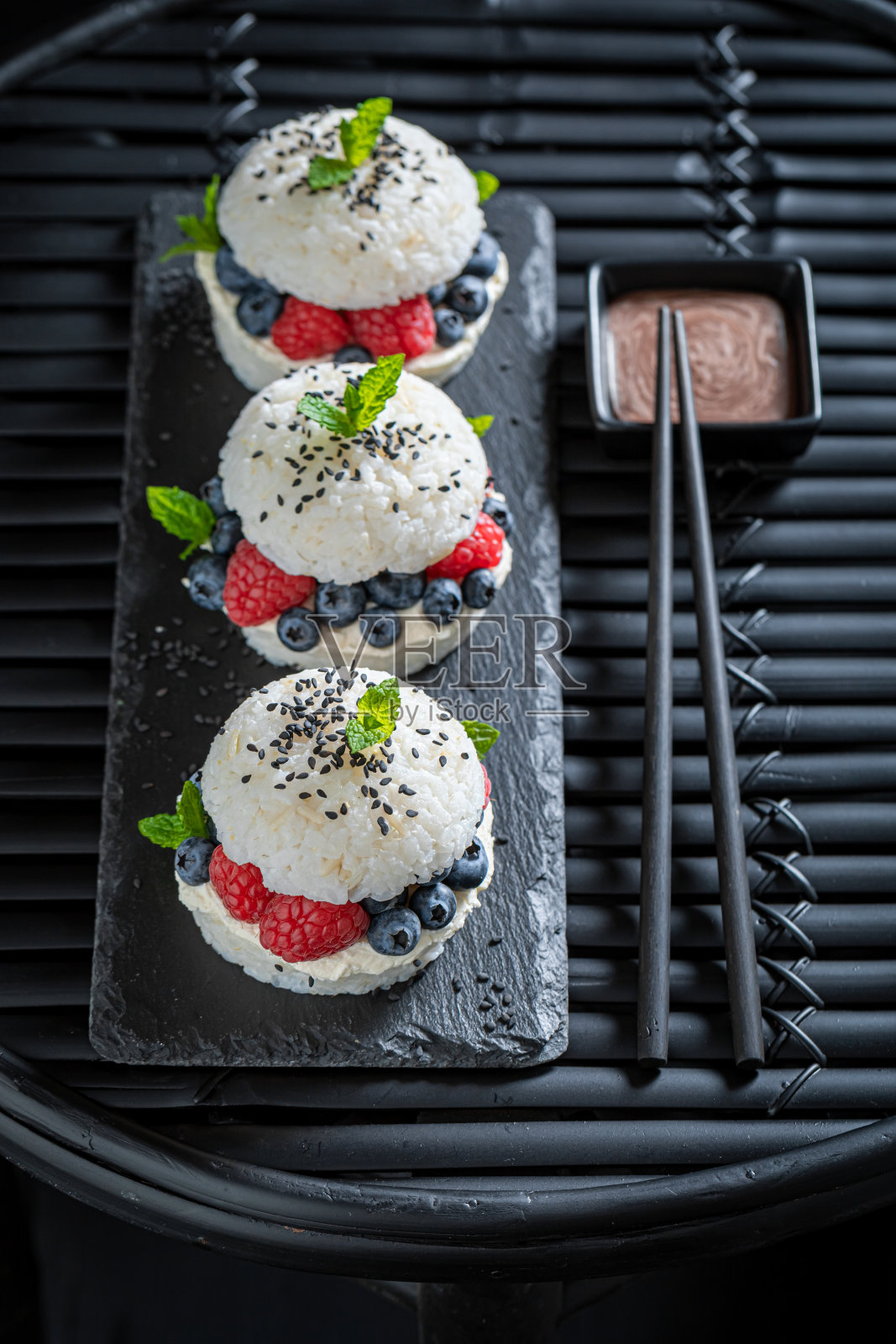 香薰寿司汉堡与浆果和马斯卡彭在黑暗的盘子。照片摄影图片