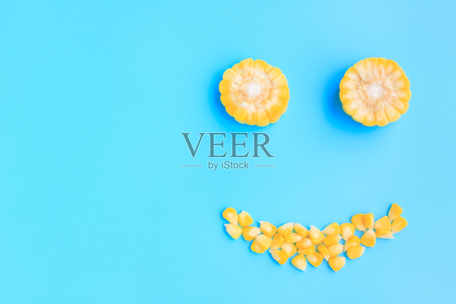 蓝色背景上的黄色玉米棒切片和种子笑脸照片摄影图片