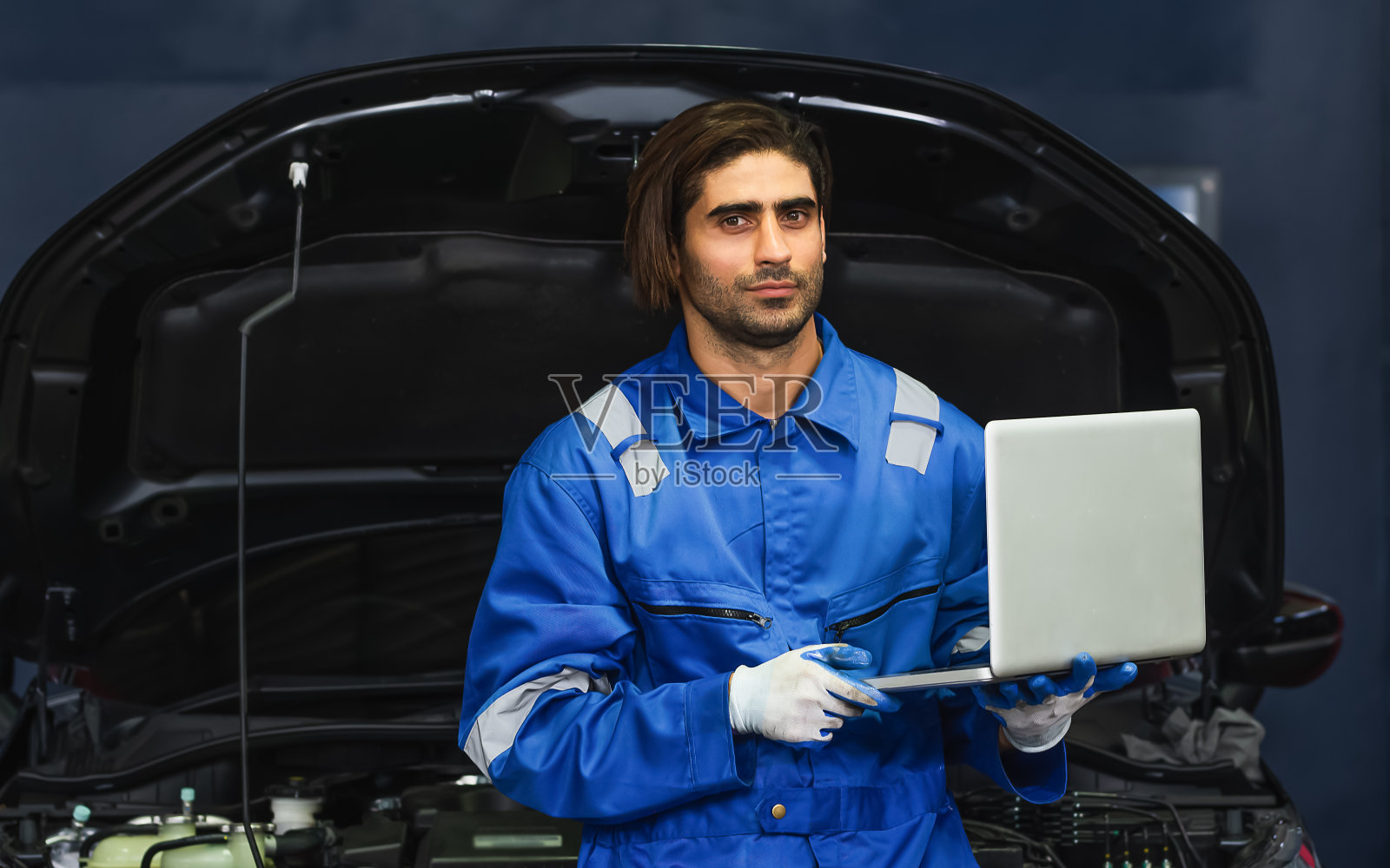 肖像成人身穿制服，手持笔记本电脑，站在汽车维修服务中心或商店进行修理、检查、检查汽车发动机的专业英俊白人男性机械师。照片摄影图片