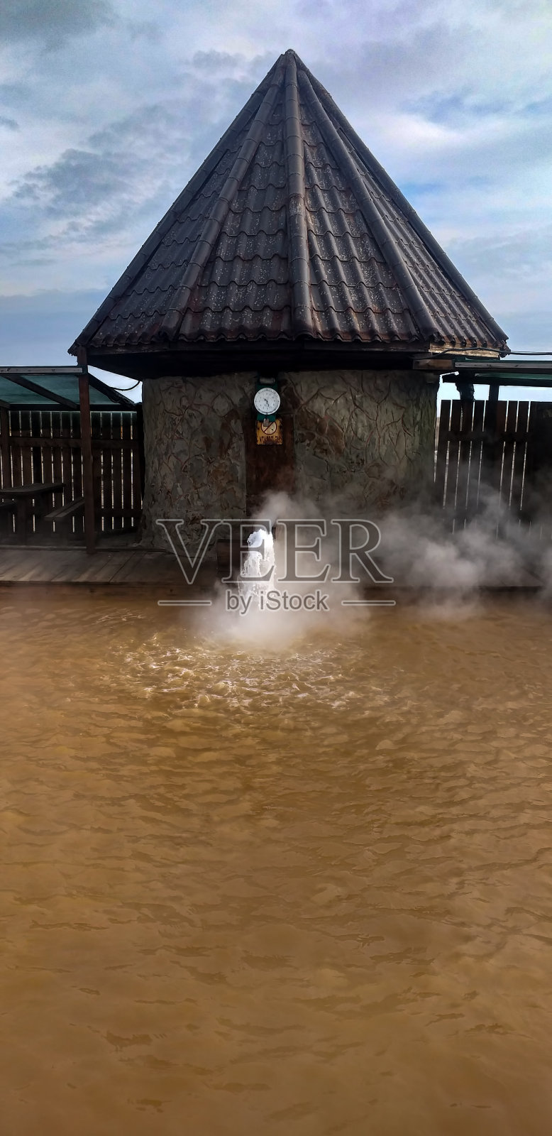 热水池，橙色的水和喷泉，背景是一间小屋和栅栏照片摄影图片