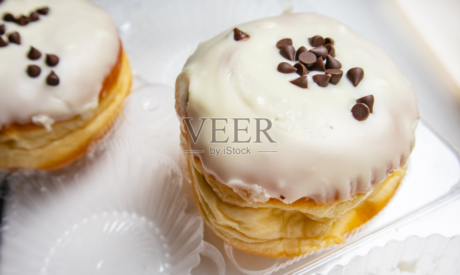 两个美味的甜甜圈，白色的背景，糖霜和巧克力片，放在透明的塑料容器里照片摄影图片