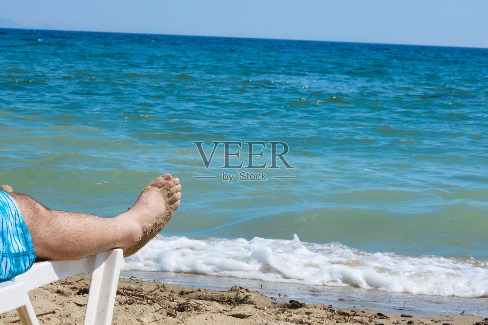 男人在沙滩躺椅上晒太阳，可以看到波浪形的蓝色海景。照片摄影图片