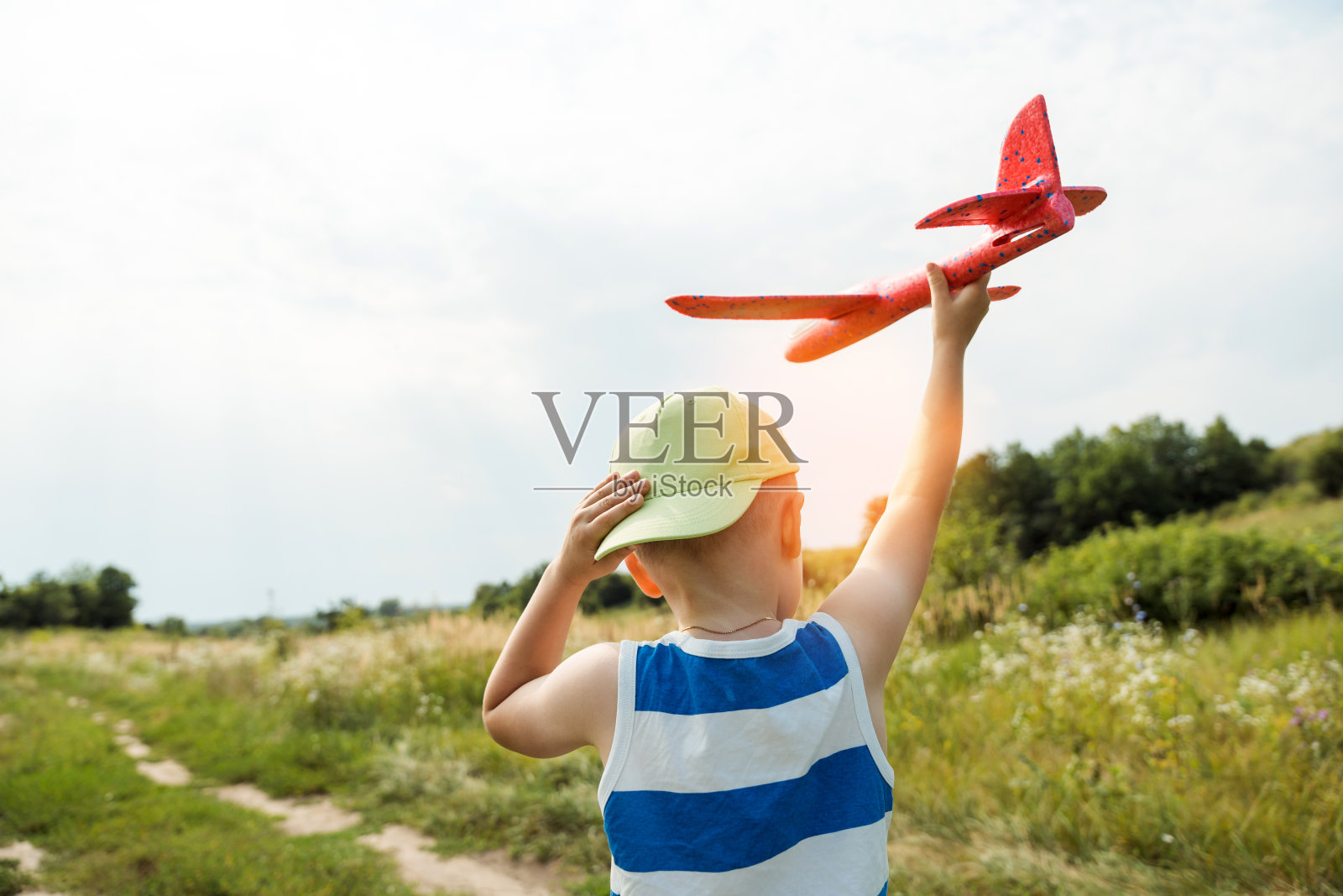 男孩拿着玩具飞机和帽子，准备在户外把飞机发射上天。快乐童年，做梦概念。照片摄影图片