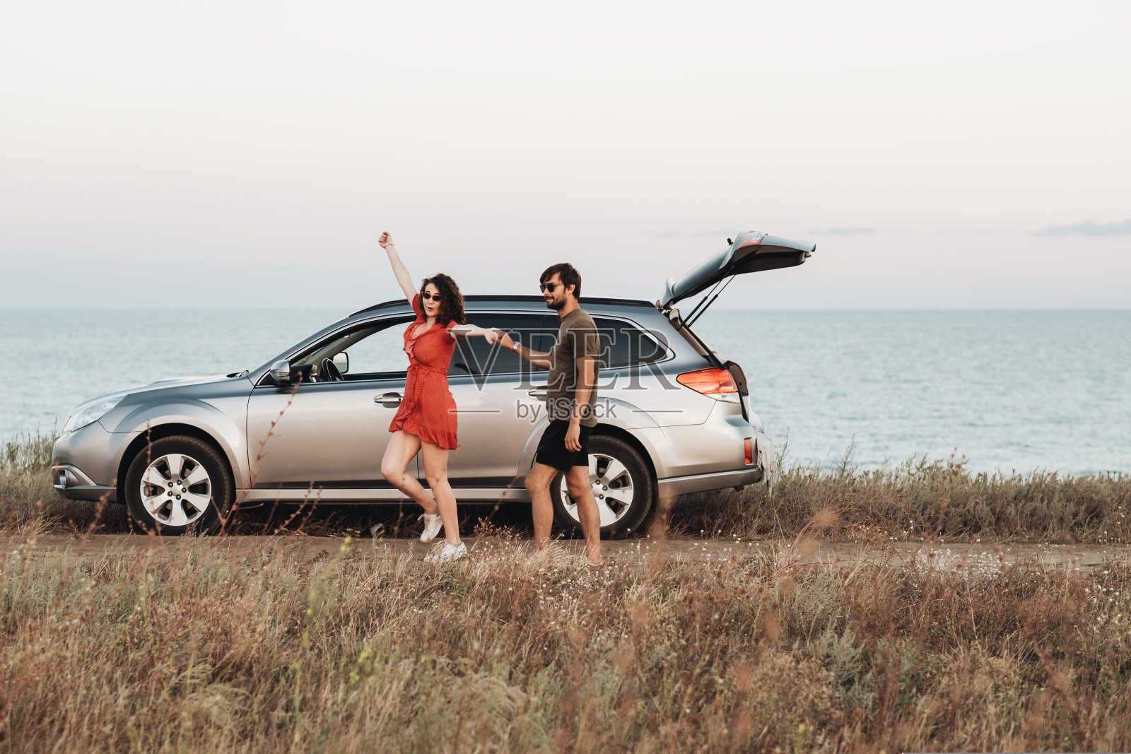 青年夫妇在大海的背景下玩得很开心，男人和女人在日落时享受他们的SUV车附近的公路旅行照片摄影图片