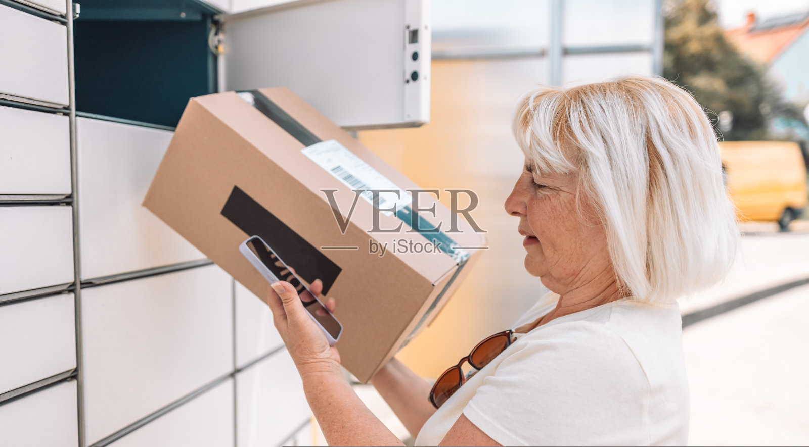 50多岁的白人妇女从户外的自动邮政终点站领取包裹。照片摄影图片