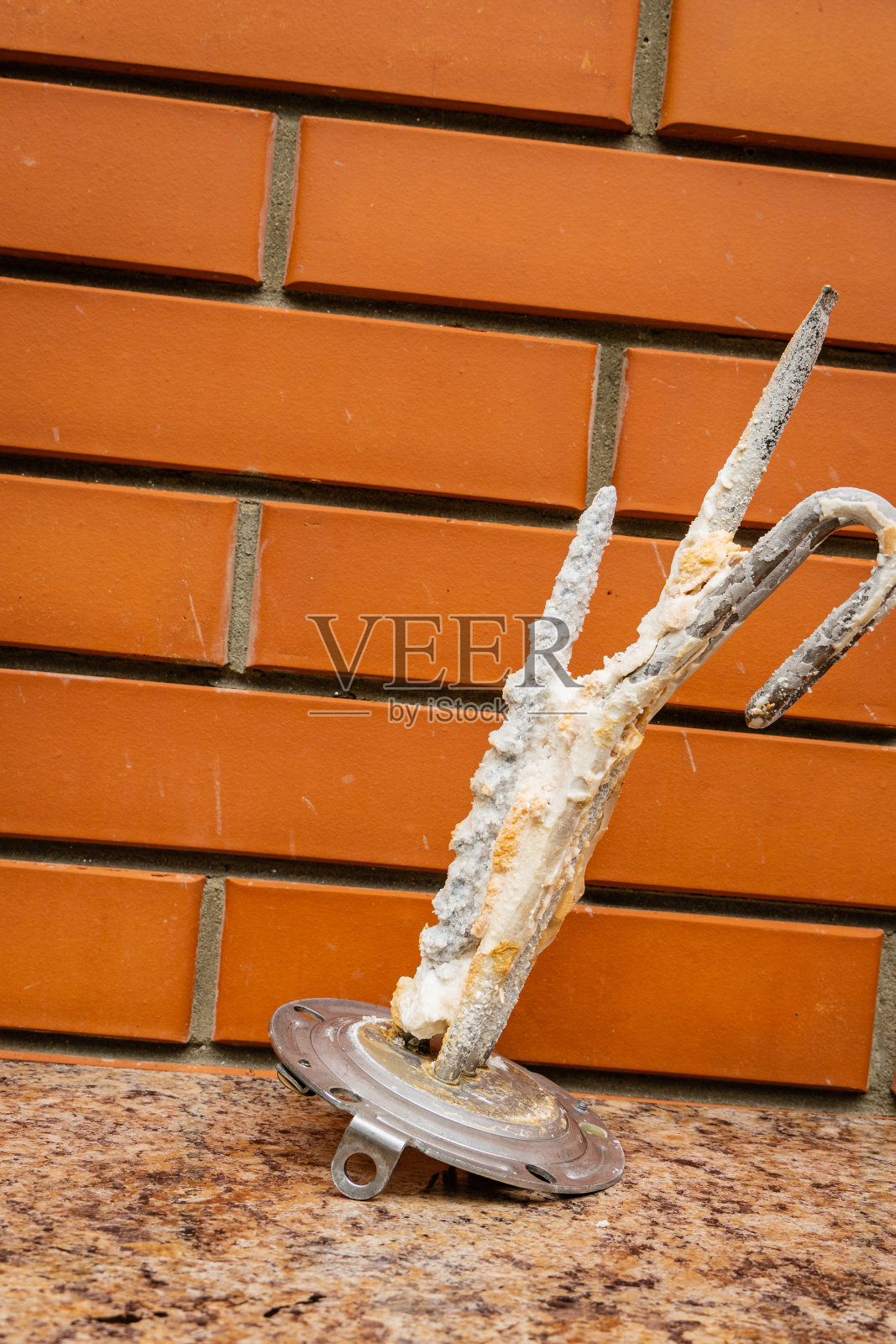 热水器维修。热水器电热元件上有浮渣。特写镜头。不锈钢加热元件和阳极上有石灰沉积。模糊砖墙背景上的加热元件。照片摄影图片