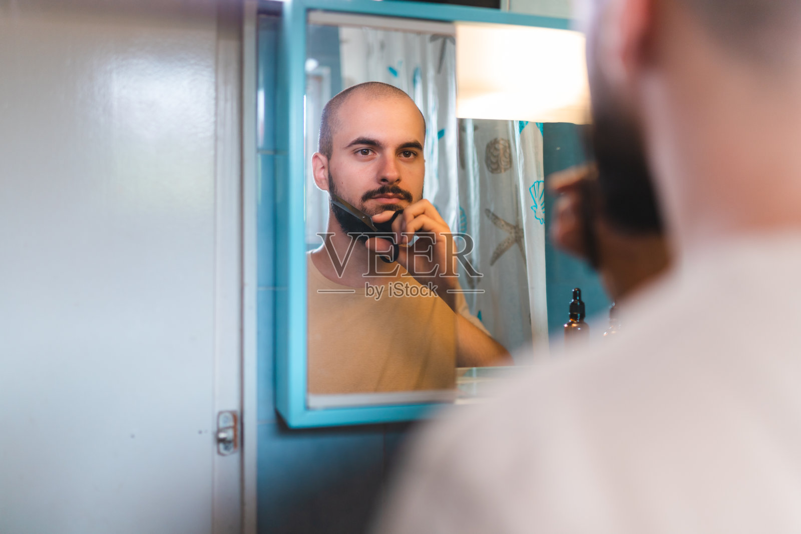 一个秃顶的年轻人在浴室镜子前用剪刀修剪他的胡子的特写照片摄影图片