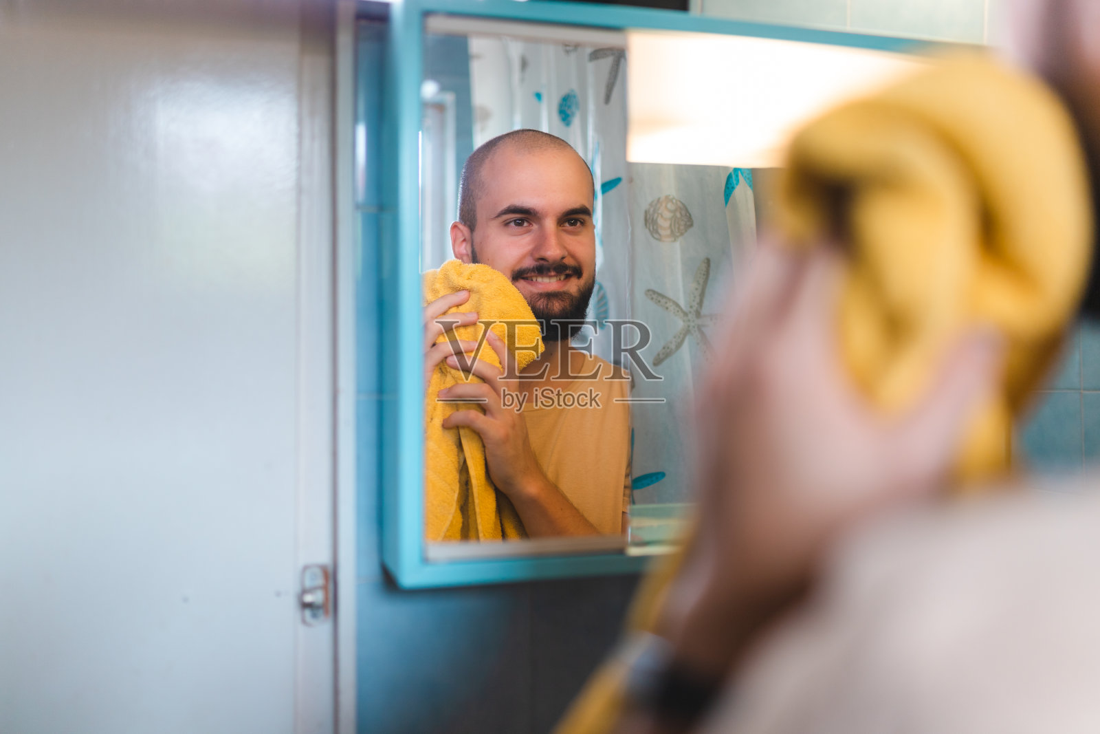 一个秃顶的年轻人在浴室镜子前用毛巾擦胡子的特写照片摄影图片