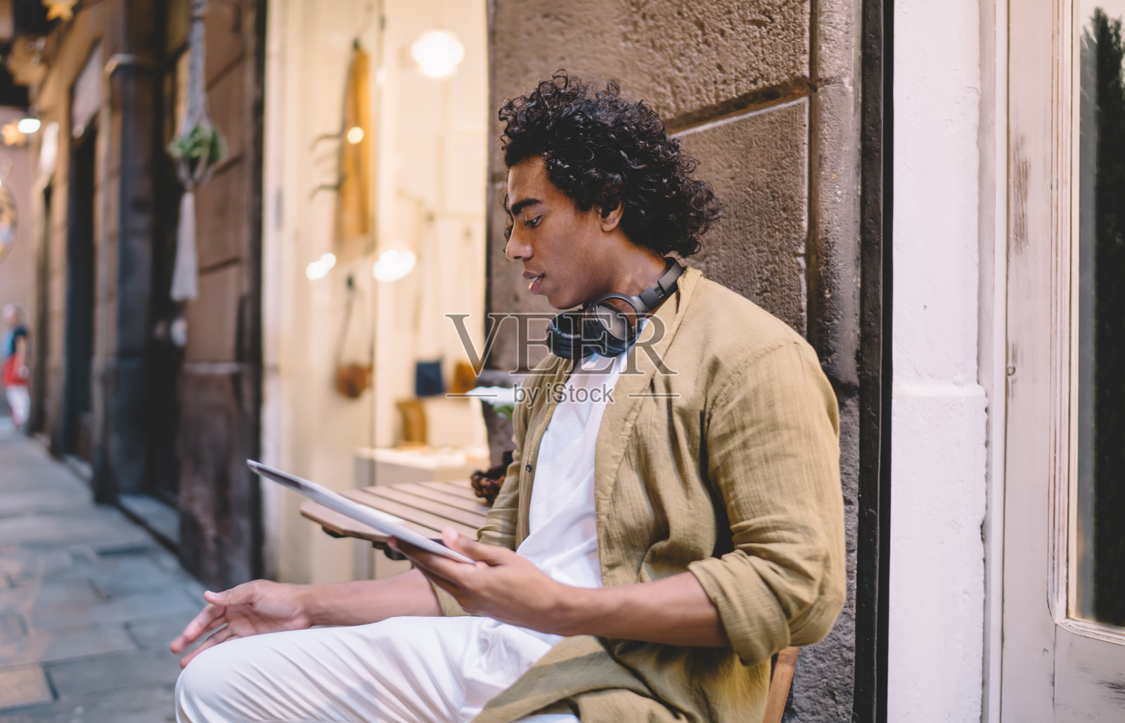 深思熟虑的男人戴着耳机和笔记本电脑坐在街边的石凳上照片摄影图片
