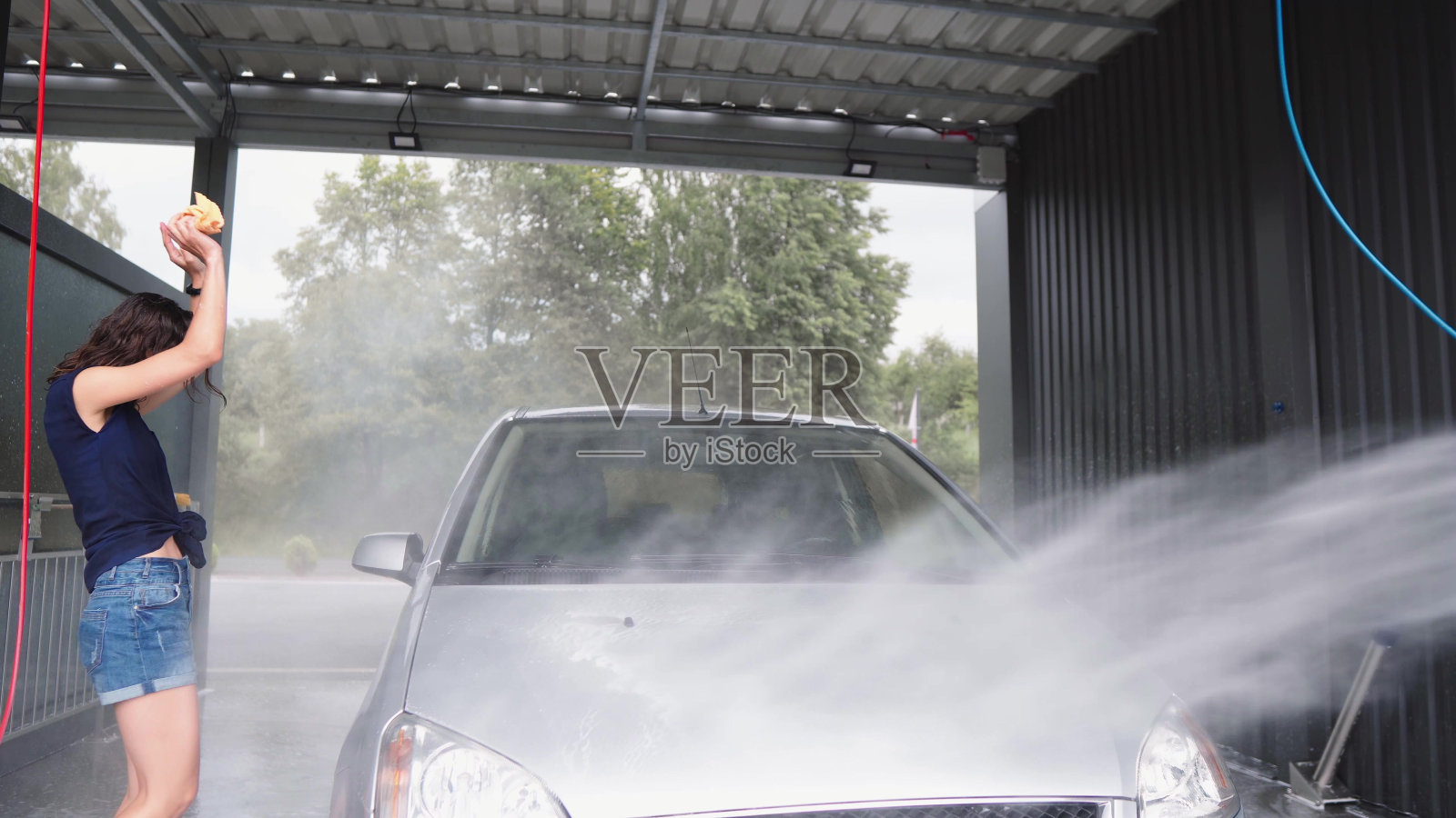 一男一女在自助洗车场。阳光明媚的日子里，一对快乐的情侣在院子里洗车玩耍。女孩和男孩用泡沫和水在压力下清洗汽车，然后用抹布擦拭。照片摄影图片