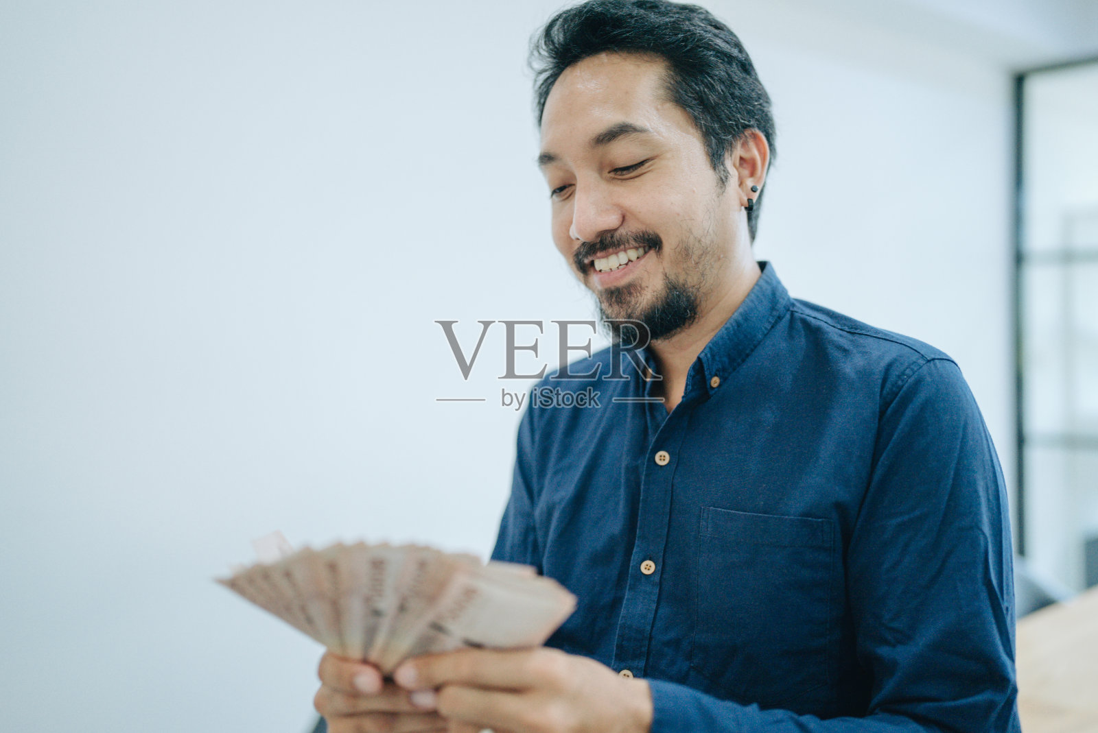 亚洲男子手里拿着泰国钞票，脸上带着幸福的笑容照片摄影图片