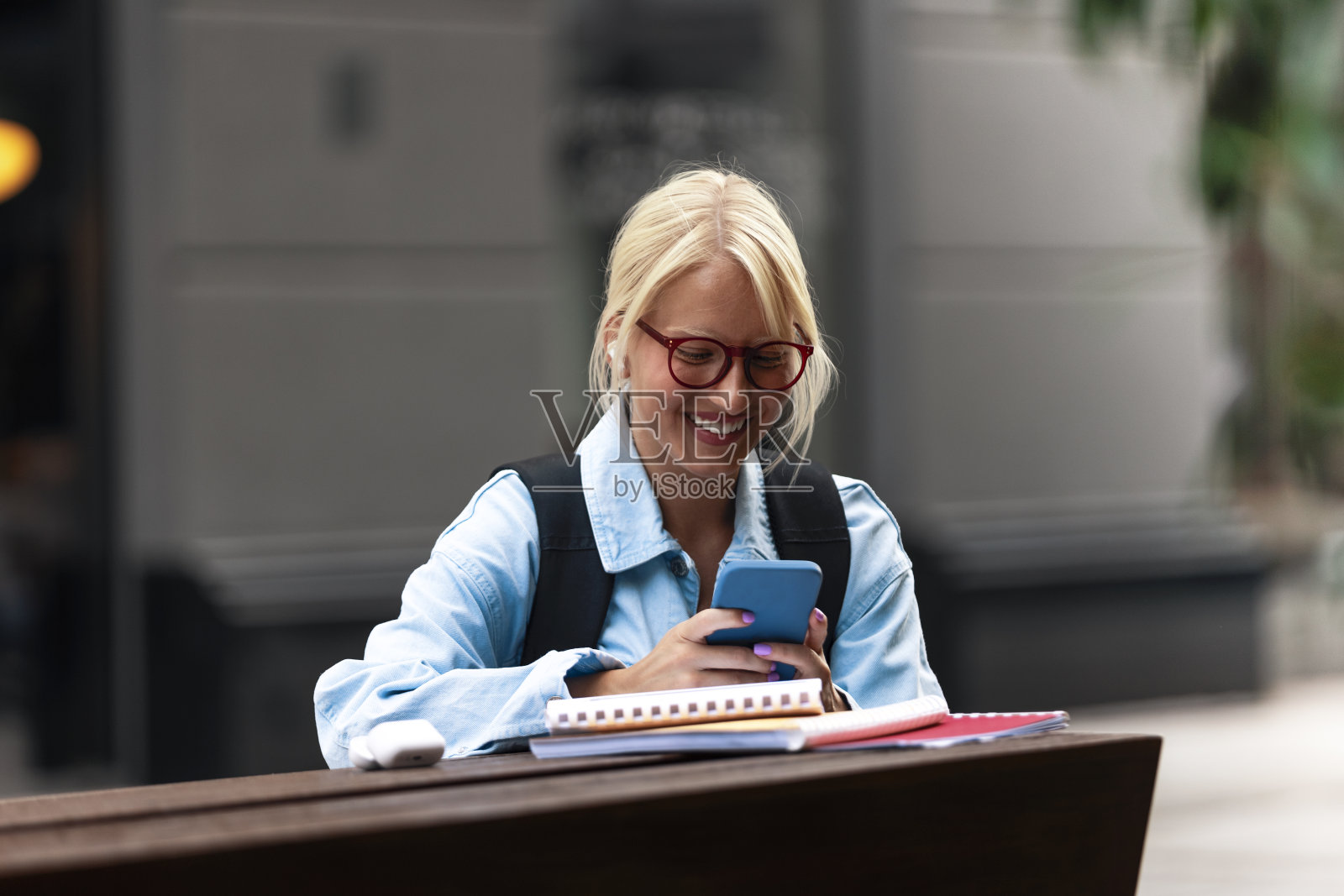 一个微笑的女学生坐在外面，用她的智能手机发短信。照片摄影图片