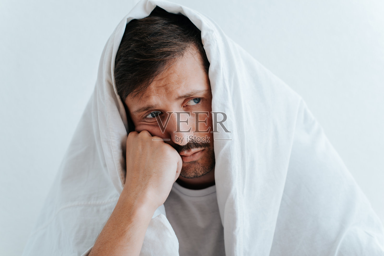 抑郁、忧郁、悲伤，男性心理健康概念。孤独疲惫的年轻人表情悲伤，经历心理问题，坐在卧室里，裹着毯子，望着远方照片摄影图片