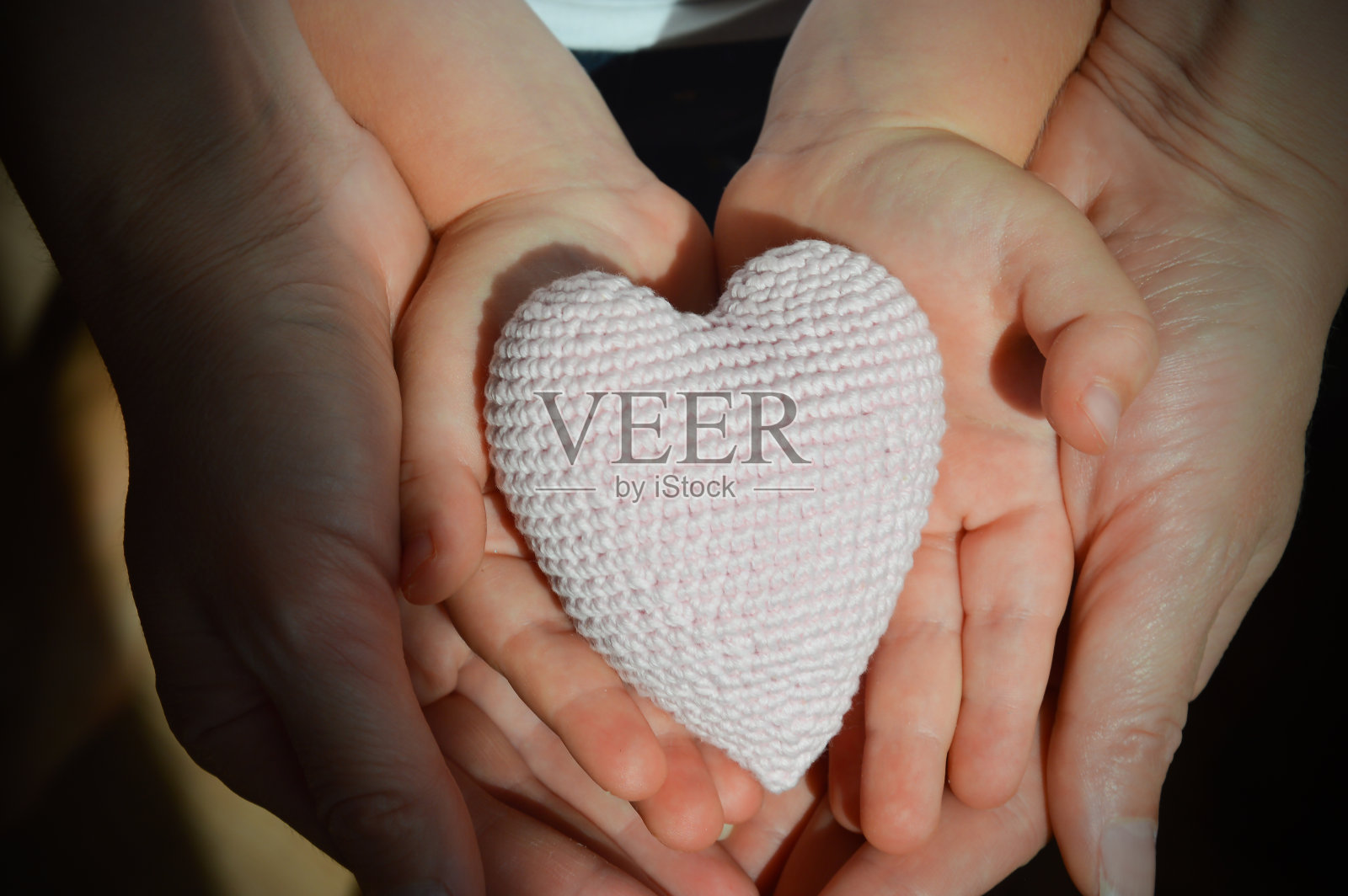 妈妈和女儿都抱着一颗小小的钩针心。一个孩子和一个女人的手。人类的手掌。爱。设计背景。照片摄影图片