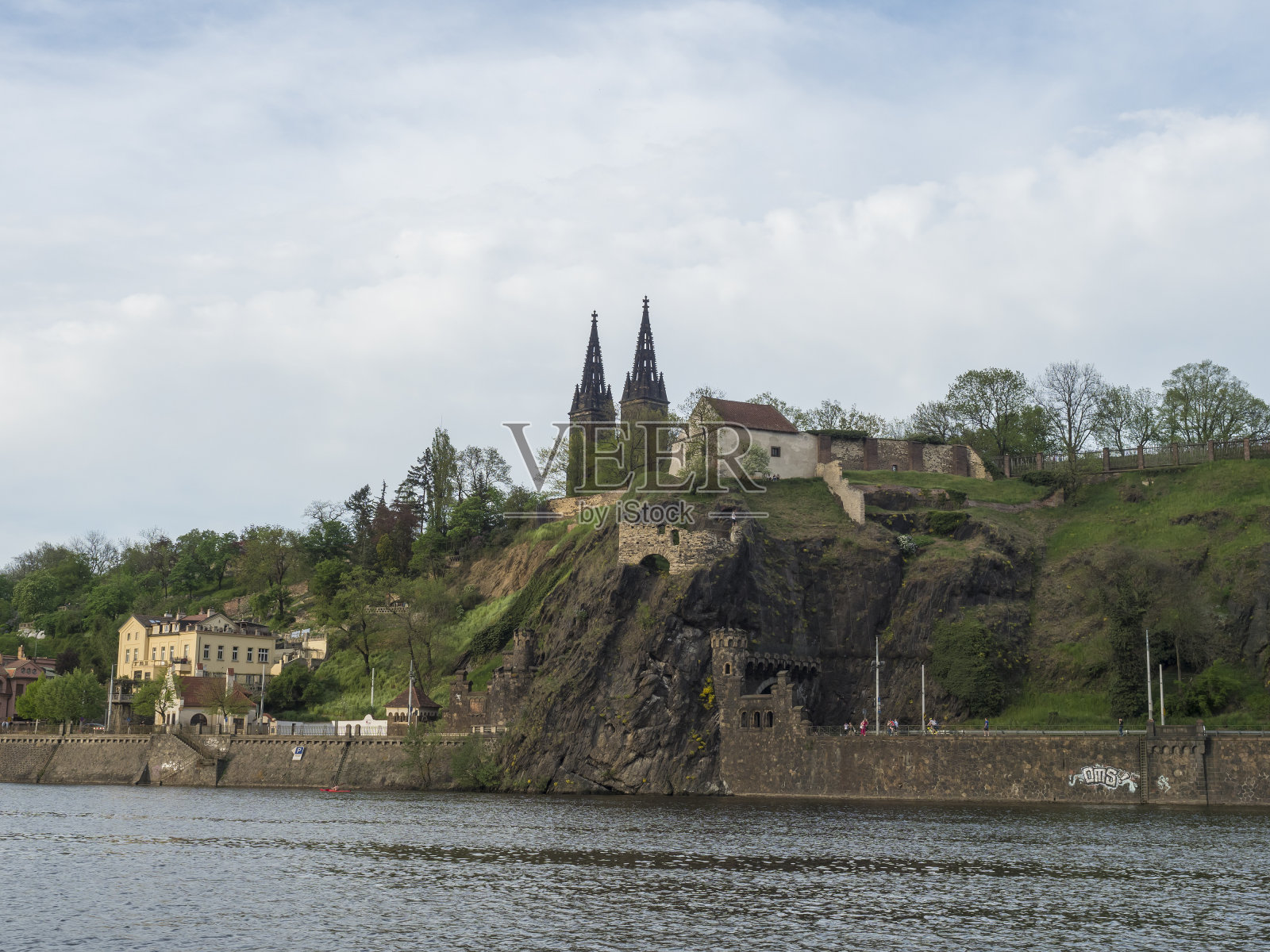 在伏尔塔瓦河岸，可以看到历史悠久的维瑟拉德堡，圣彼得和保罗大教堂，哥特式教堂坐落在绿色的山丘和岩石上，布拉格，捷克共和国，春天。照片摄影图片