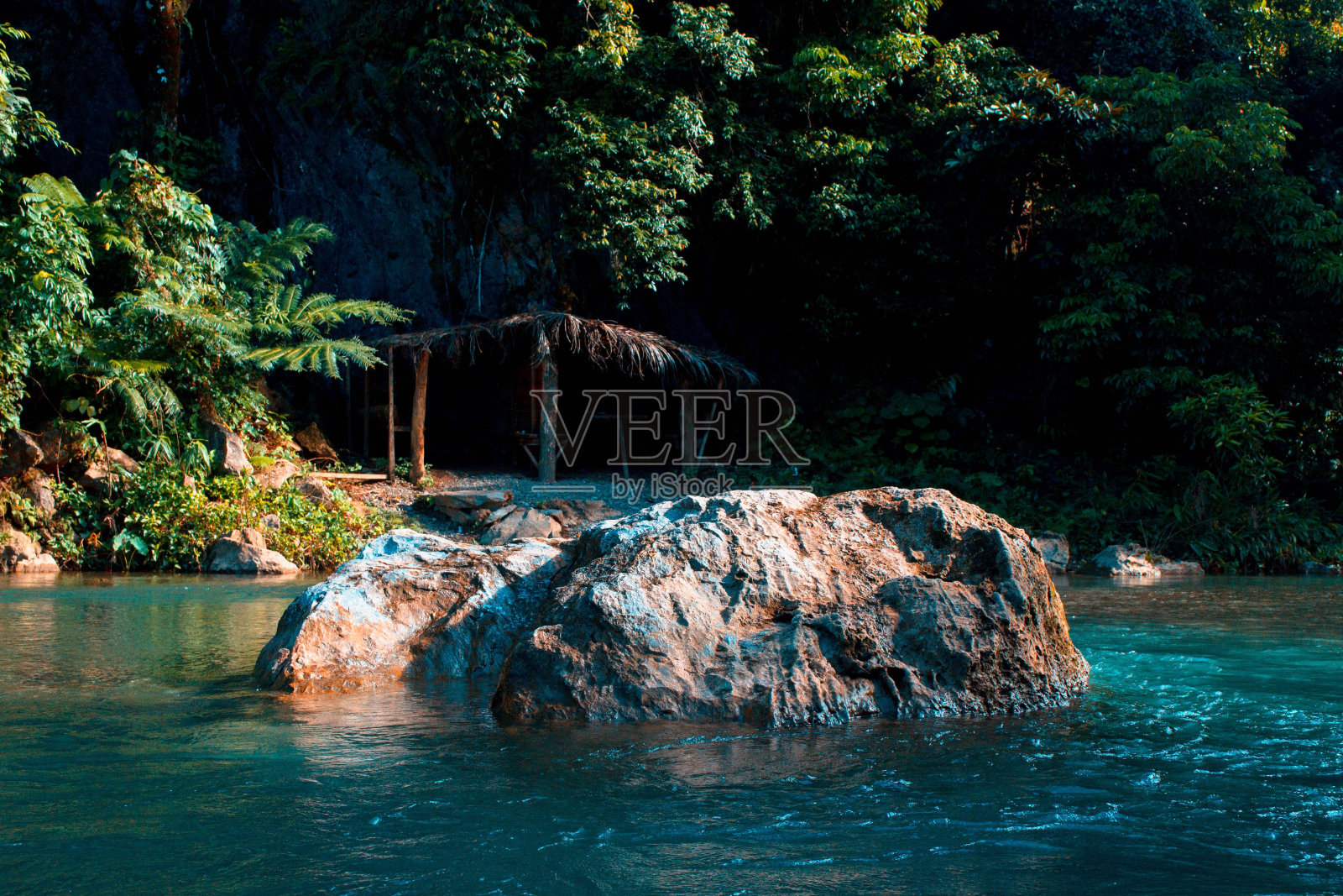 美丽的热带竹屋在海滩和一个巨大的岩石在水中照片摄影图片