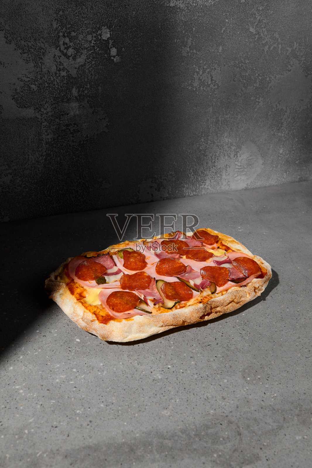 传统的意大利肉披萨，黑色底色搭配意大利辣香肠和培根。灰色石桌上的肉钉，阴影很硬。罗马披萨配意大利辣香肠和培根。Pinsa菜单。照片摄影图片