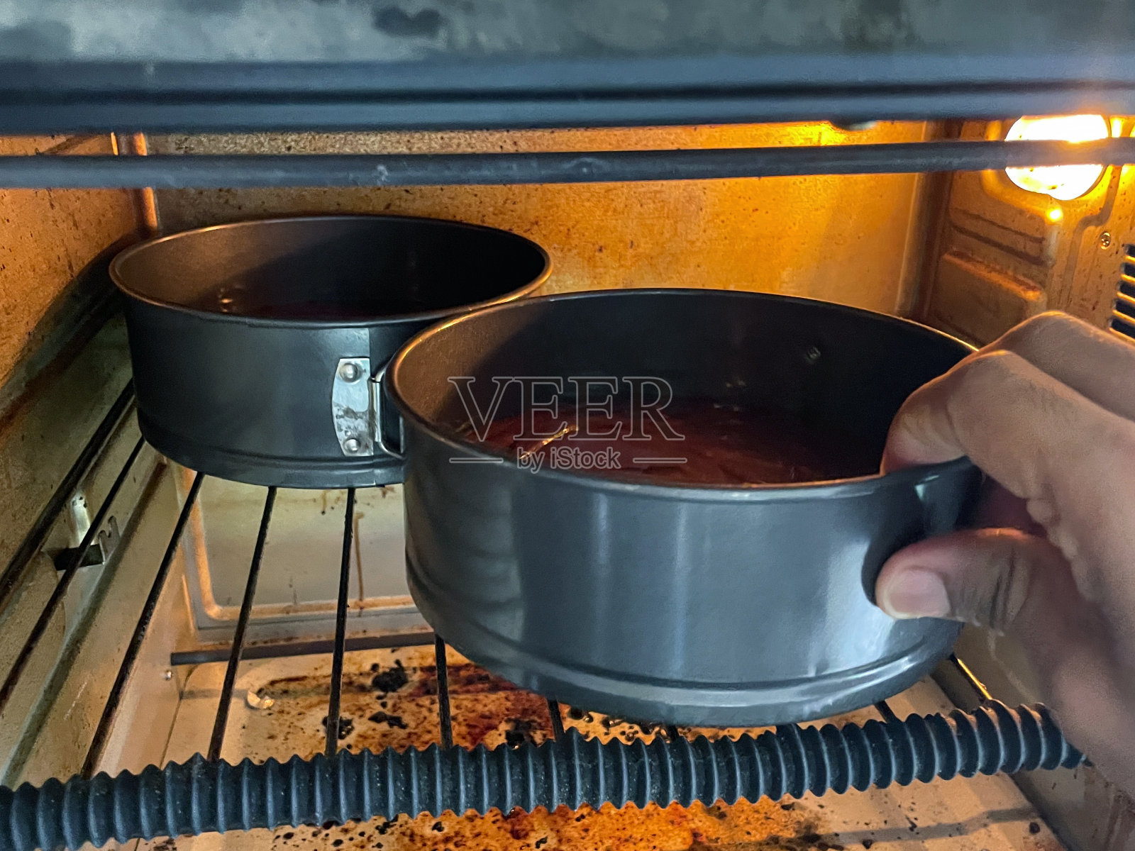 两个不粘蛋糕罐的巧克力维多利亚海绵蛋糕面糊，混合黄油，糖，面粉和可可放在热烤箱架上，在家烘焙照片摄影图片