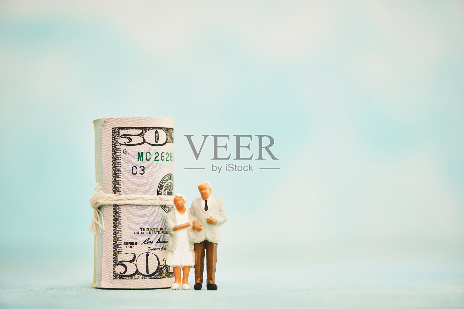 一对年长的夫妇站在一卷美元旁边。退休及退休金主题照片摄影图片