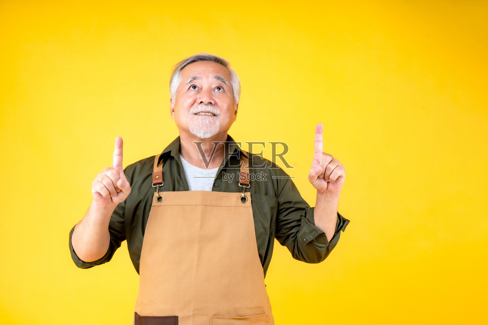 肖像迷人的亚洲退休老人留着白色的小胡子，戴着围裙指着胡子，双手临摹空间。照片摄影图片