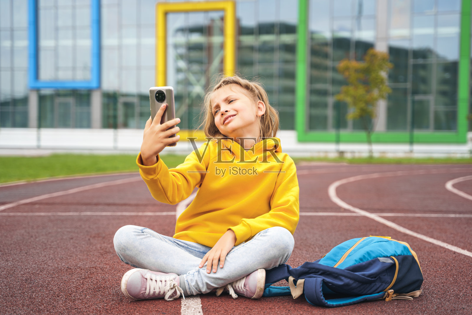 十几岁的女孩穿着卫衣带着手机，背着书包在校园里。博客录制视频博客在体育操场和体育场。和妈妈、朋友、同学聊天。在大学里休息。初等教育照片摄影图片