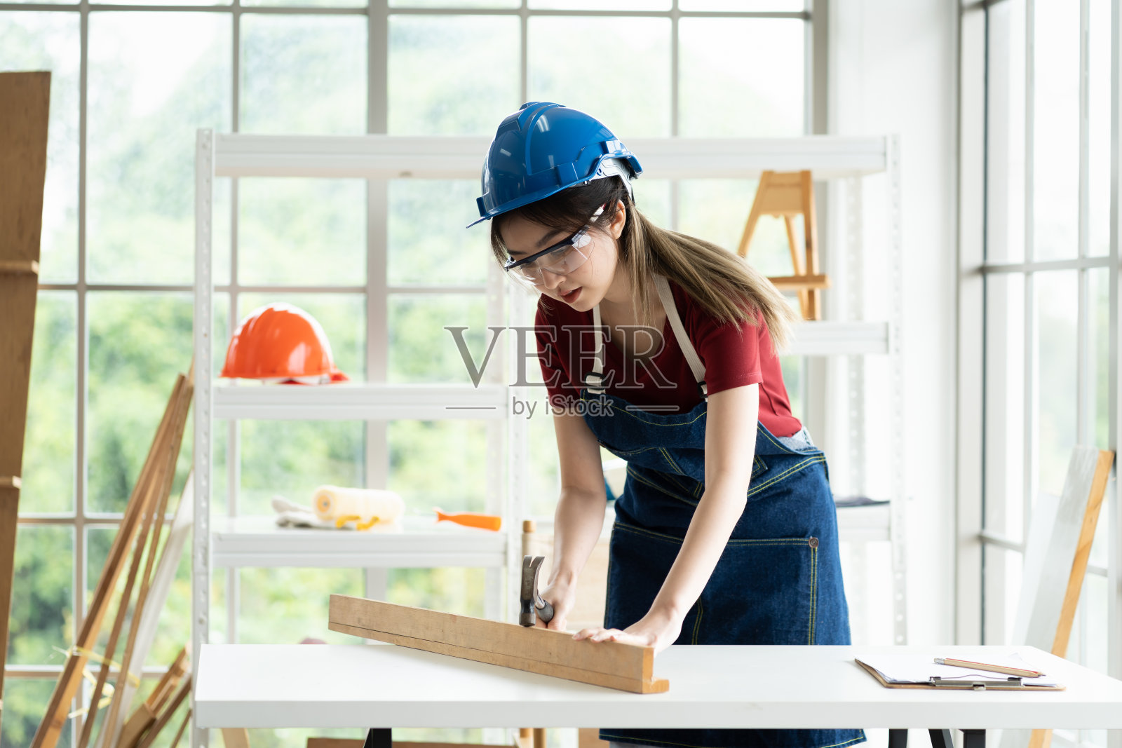年轻的亚洲女木匠在木材车间用锤子敲打木头。女细木工在木工店工作照片摄影图片