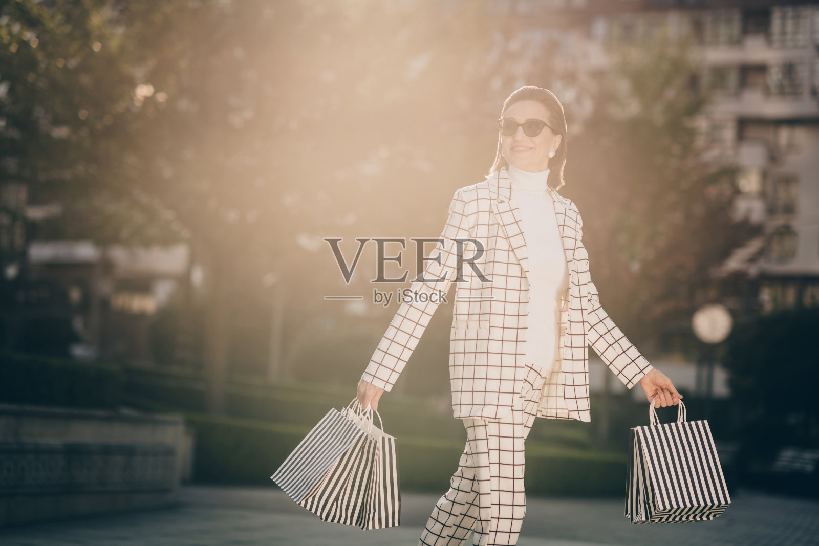 照片可爱迷人的女人穿格子夹克手臂眼镜步行购物者享受阳光外的城市住宅综合体照片摄影图片