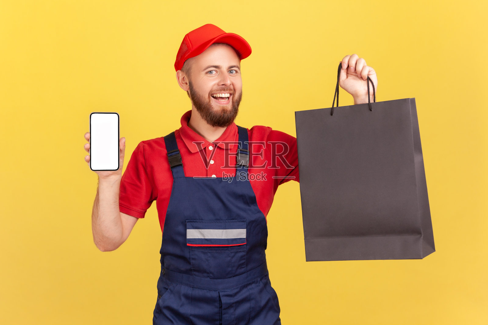 快递员拿着购物袋，展示空显示屏的智能手机，从商店送货上门。照片摄影图片