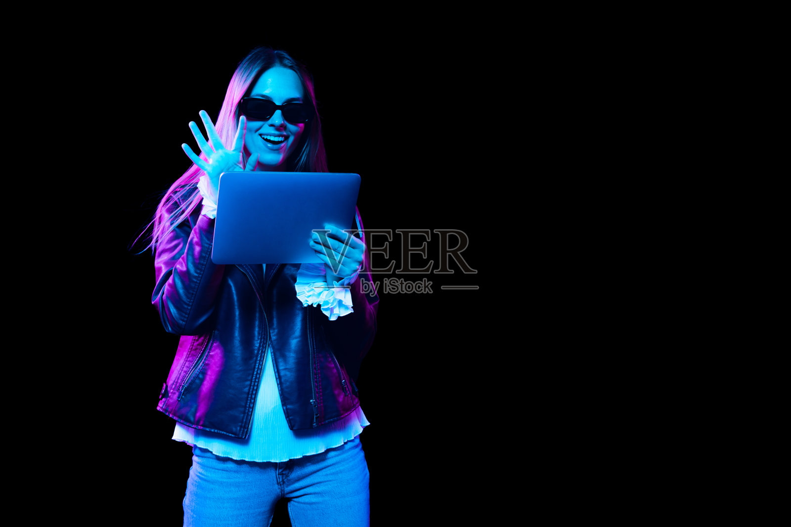 时尚年轻漂亮的女孩使用数码平板电脑隔离在黑暗的背景下霓虹灯。情感的概念，面部表情，青春，渴望。照片摄影图片