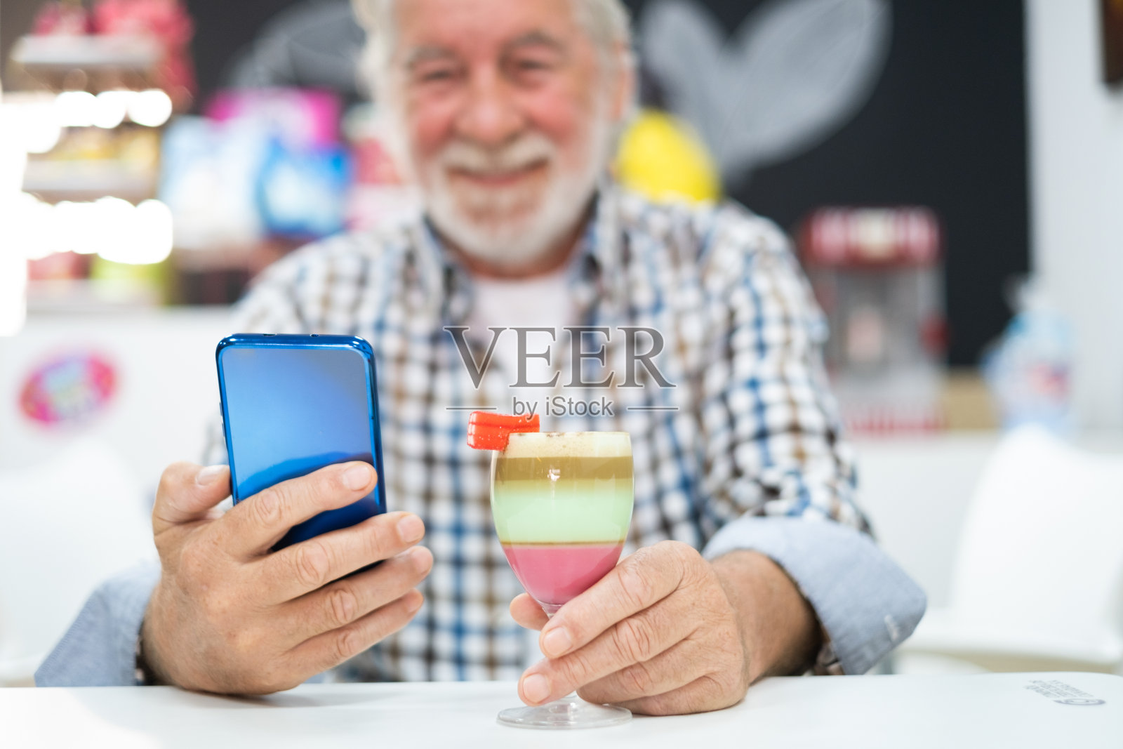 一名老人坐在加那利岛当地特产barraquito旁打电话，这是用炼乳、咖啡和利口酒调制而成的照片摄影图片