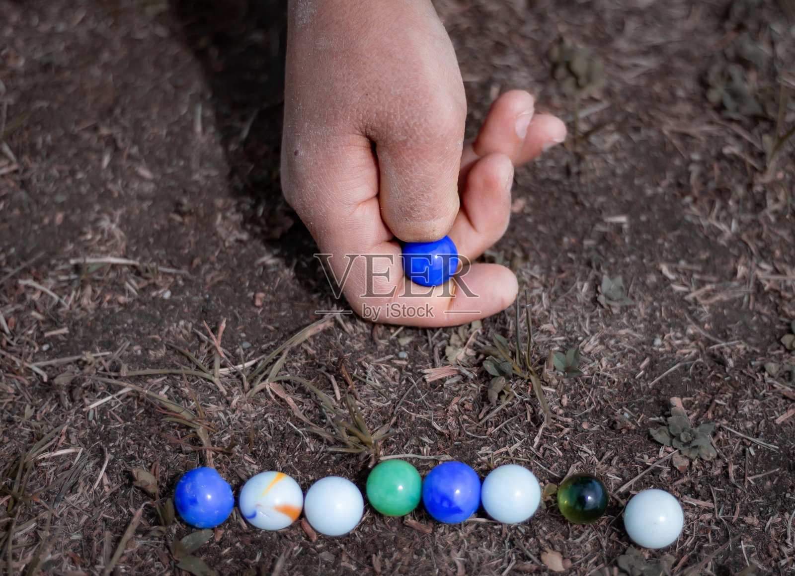 一个孩子在人行道上玩弹珠。老式玩具至今仍在使用。照片摄影图片