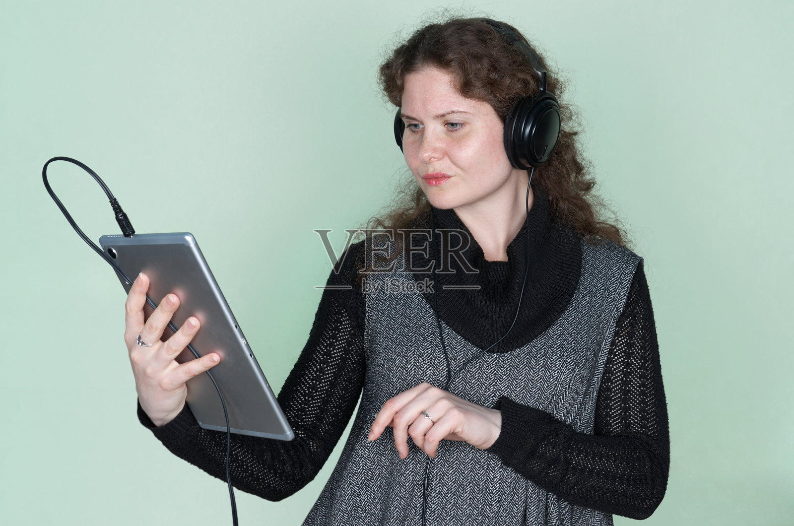 一头卷发的女子正仔细地看着手中的电子平板电脑照片摄影图片