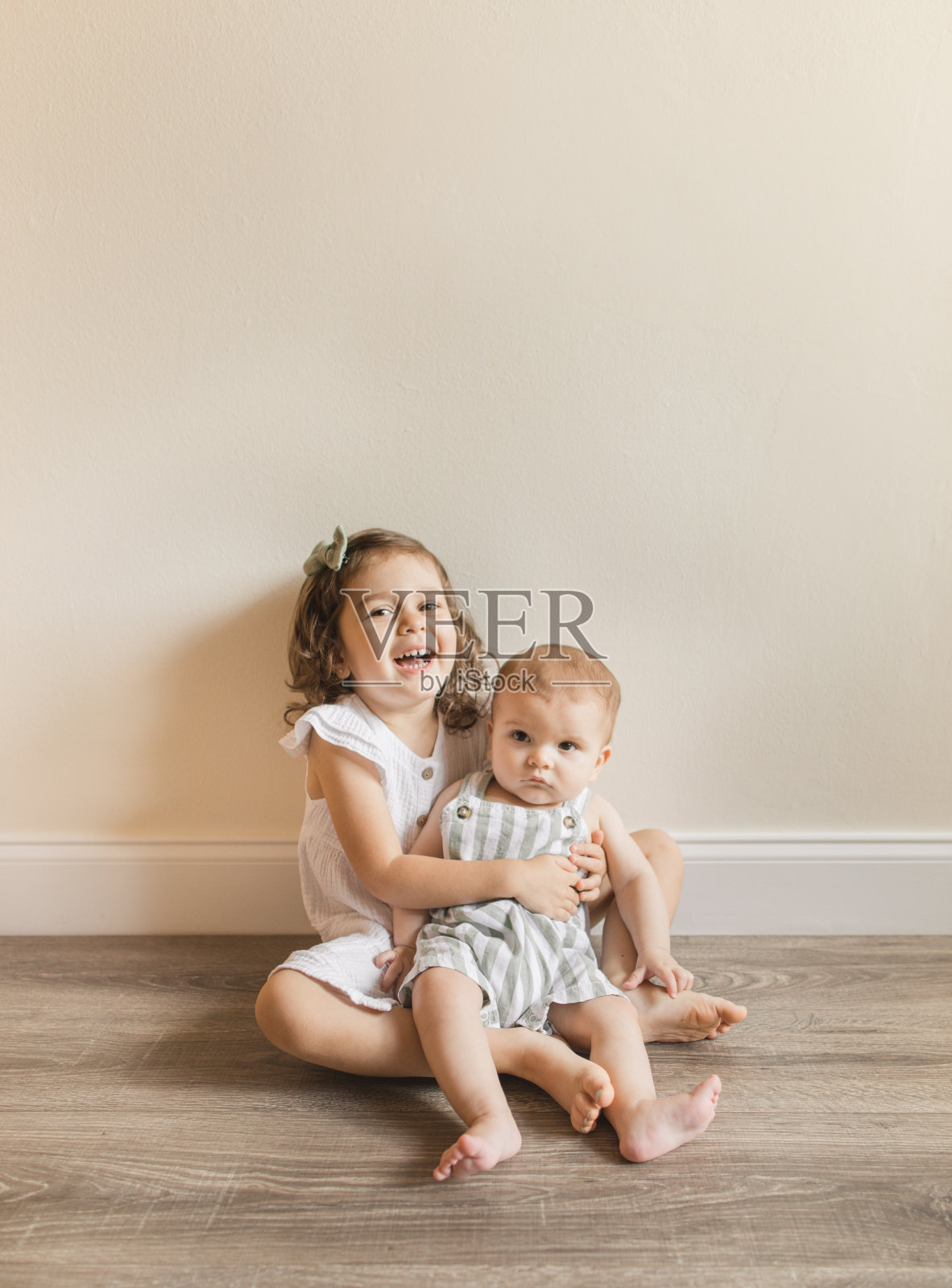 一个3岁的古巴裔美国学步女孩抱着她7个月大的弟弟，坐在家里的木地板上照片摄影图片