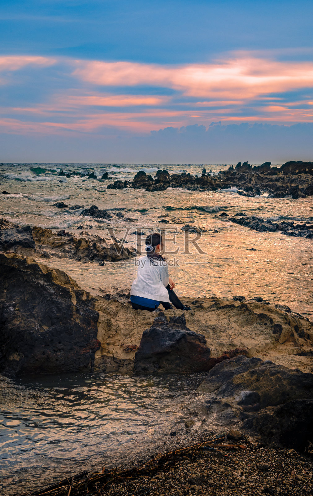 一个女孩坐在沙滩上的岩石上照片摄影图片