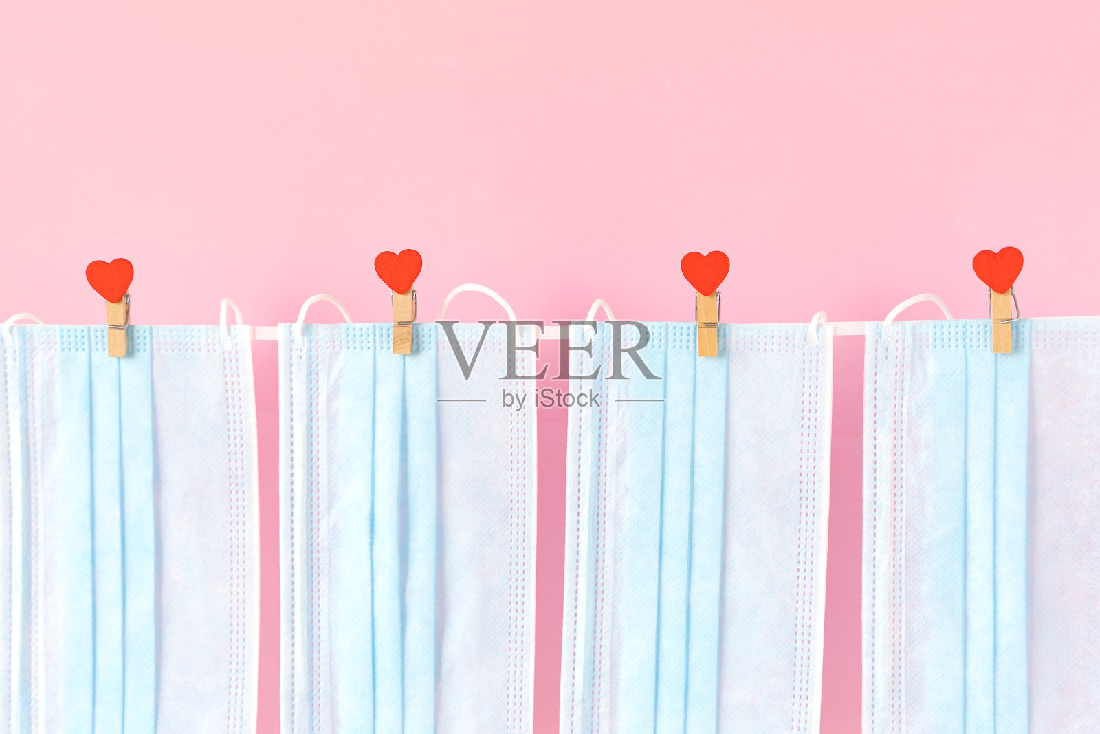 蓝色的防护口罩挂在衣夹上，绳子上系着心形图案。情人节，情侣们的情人节创造性的概念图。粉红色的背景。新的现实照片摄影图片