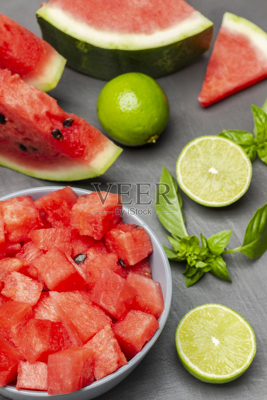 西瓜片，酸橙半片，罗勒小枝放在桌上。西瓜切片放入碗中。照片摄影图片