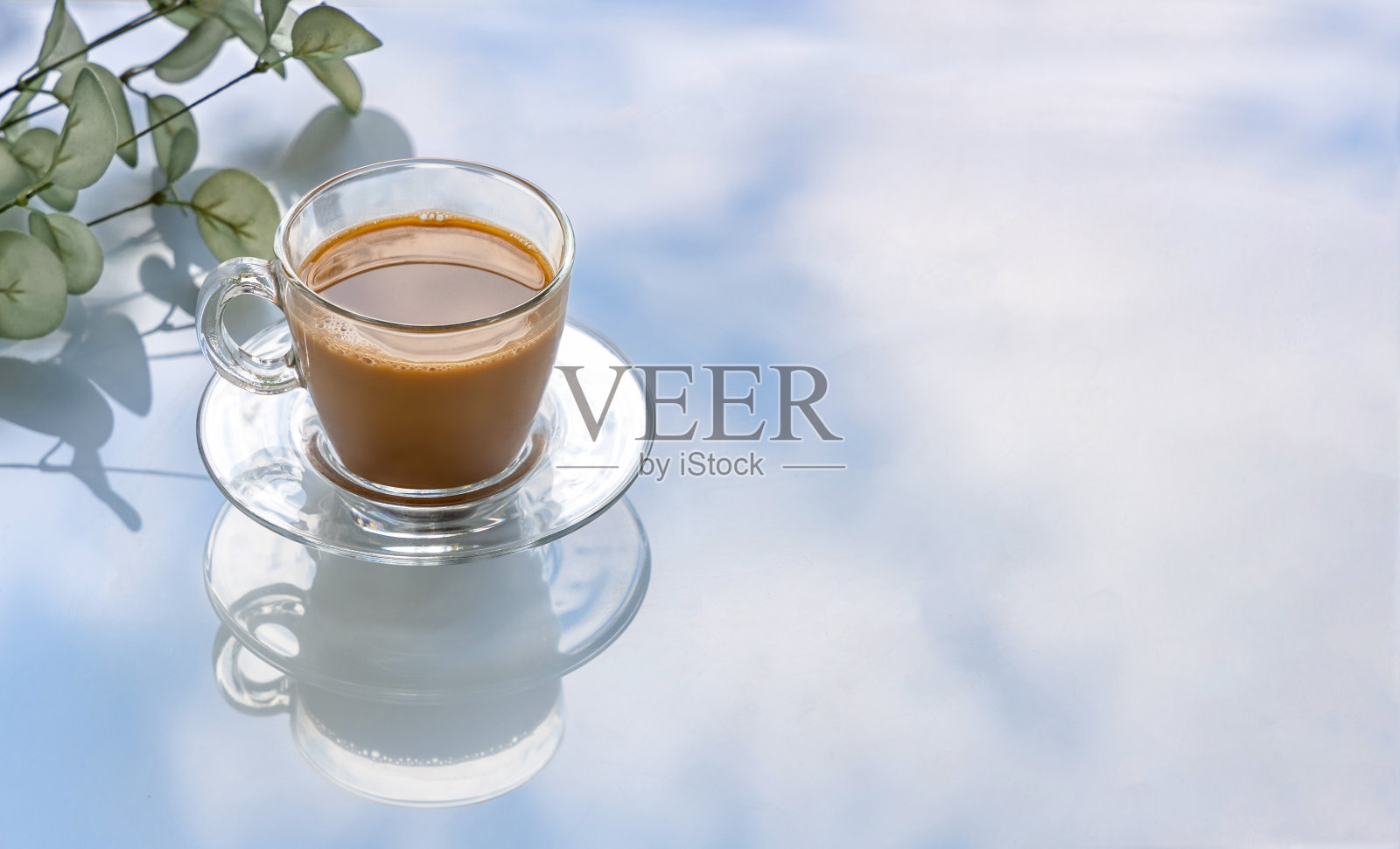 新鲜的咖啡加牛奶在一个透明的玻璃杯子上反射的背景反射天空与云照片摄影图片