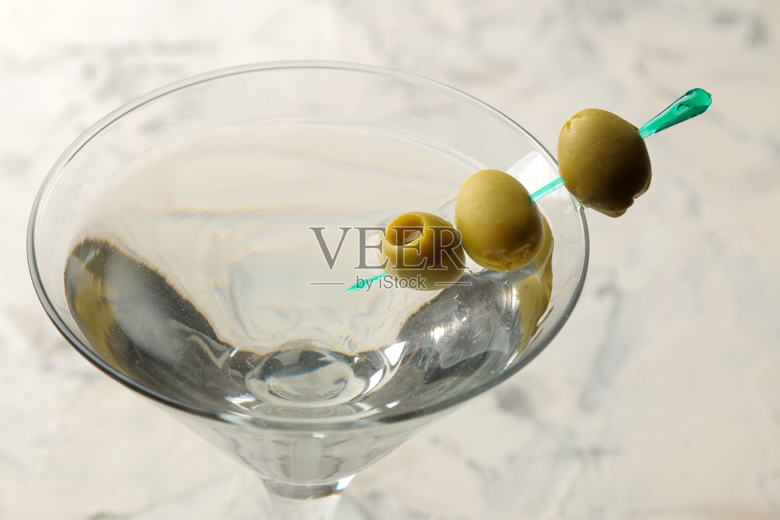 马提尼。酒精饮料马提尼加橄榄在一个杯子里，在酒吧柜台上的一个明亮的背景。酒吧库存。鸡尾酒照片摄影图片