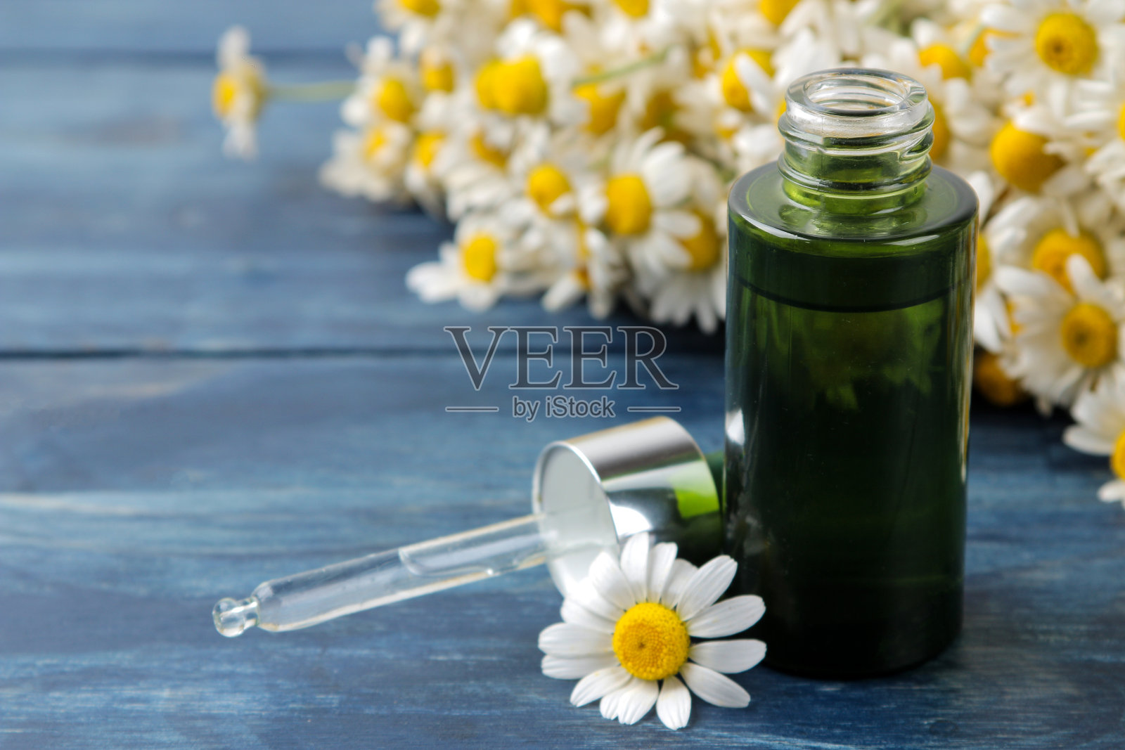 药用洋甘菊和洋甘菊提取物装在瓶子里。甘菊花的油。芳香疗法。一种药物。在一张蓝色的木桌上。特写镜头照片摄影图片