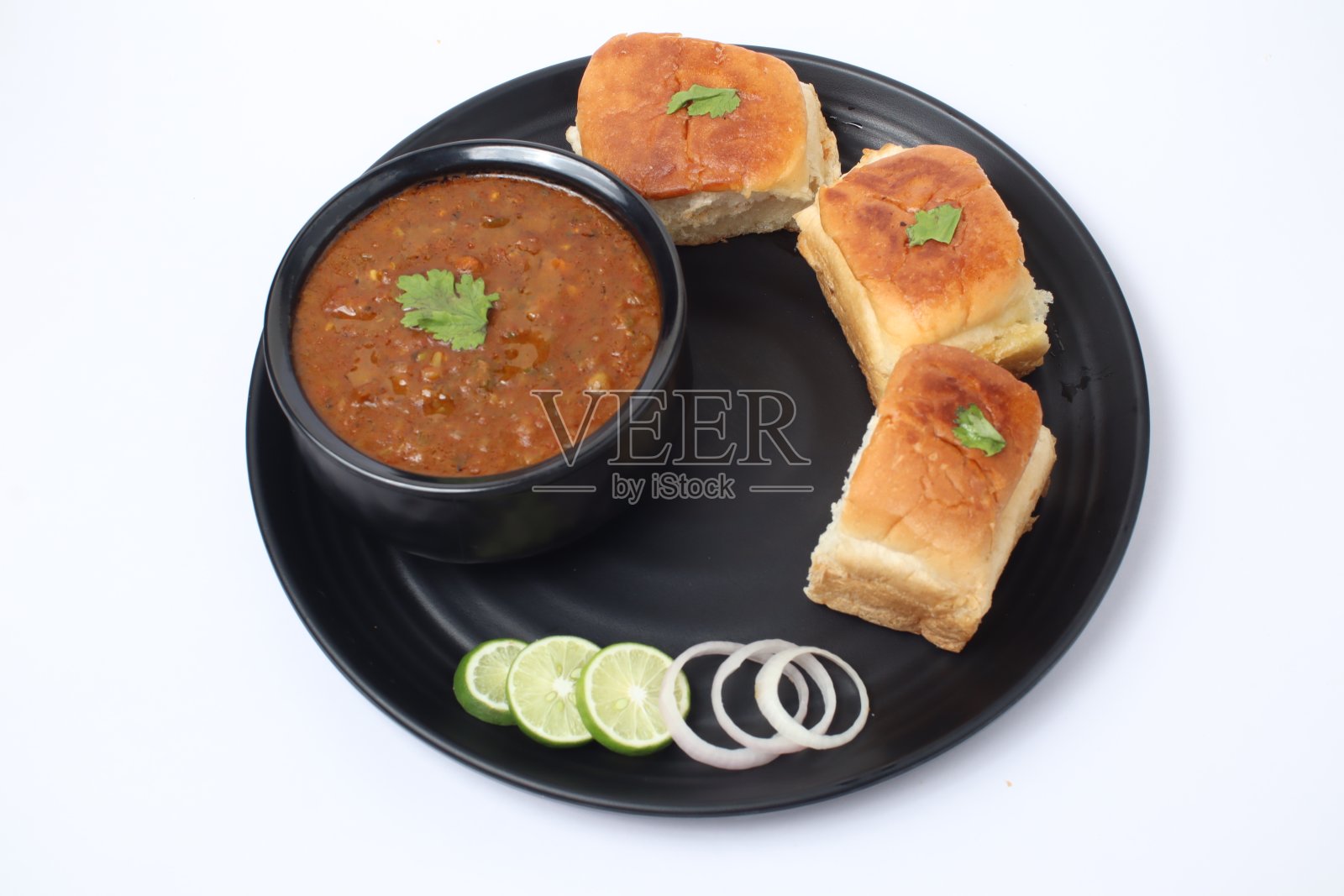 来自孟买的印度快餐，蔬菜咖喱配软面包卷，盛在黑色盘子里，白色背景上有洋葱和柠檬照片摄影图片