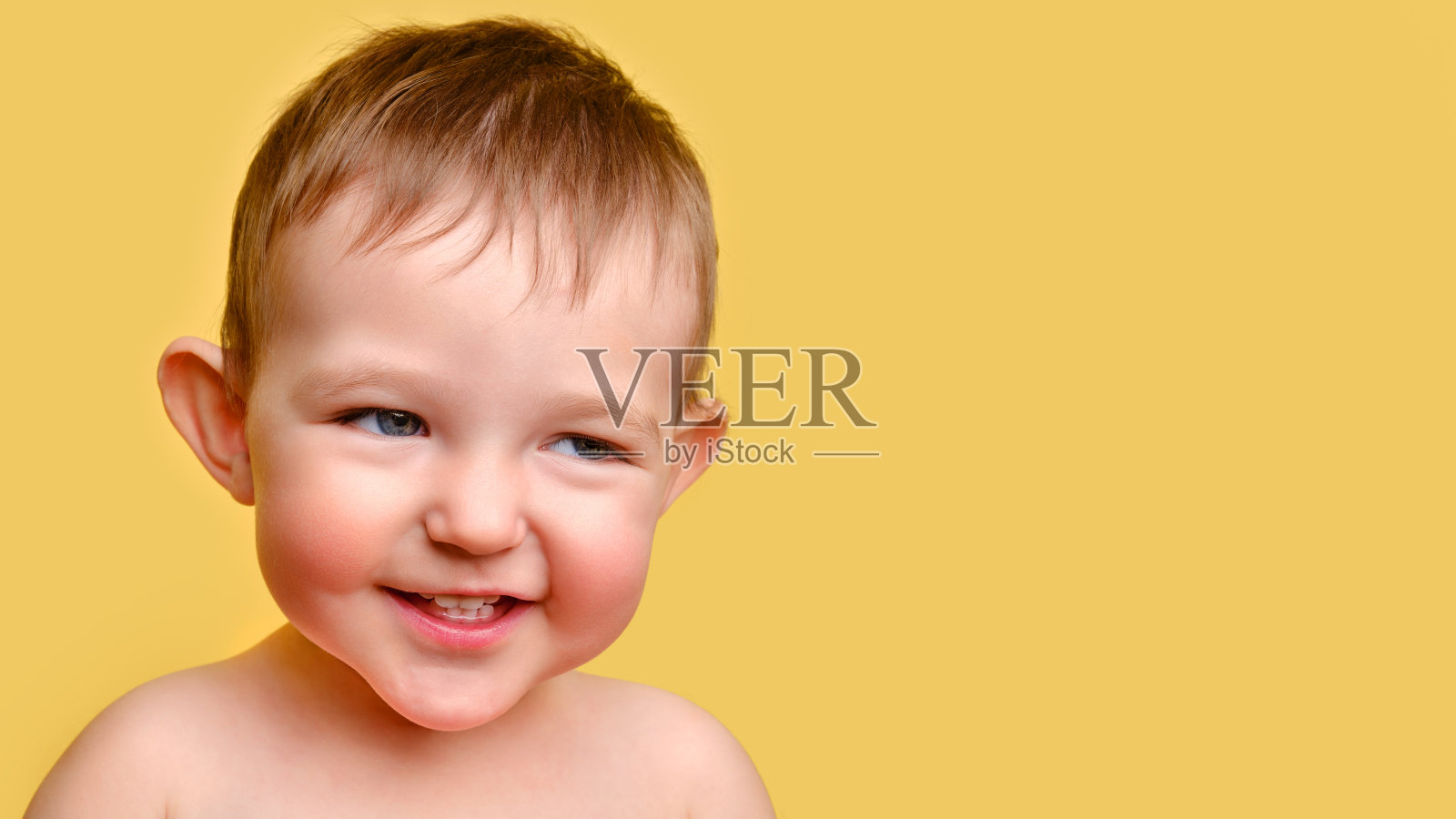 淘气的小孩，工作室黄色背景，拷贝空间。一个脸颊通红的阴险孩子的画像。孩子一岁两个月大照片摄影图片