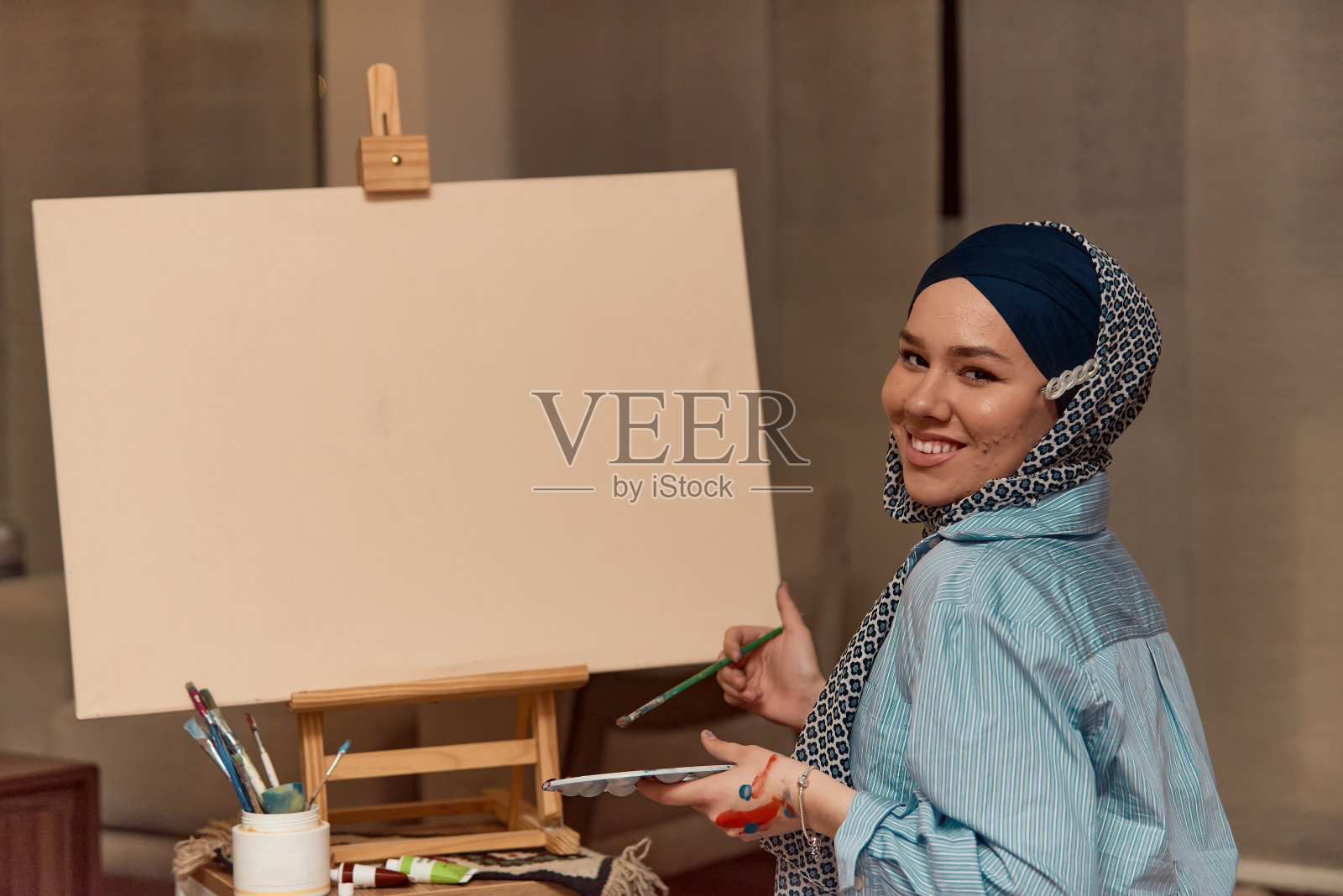 一名戴着头巾的妇女用画笔和蛋彩画在画布上作画照片摄影图片