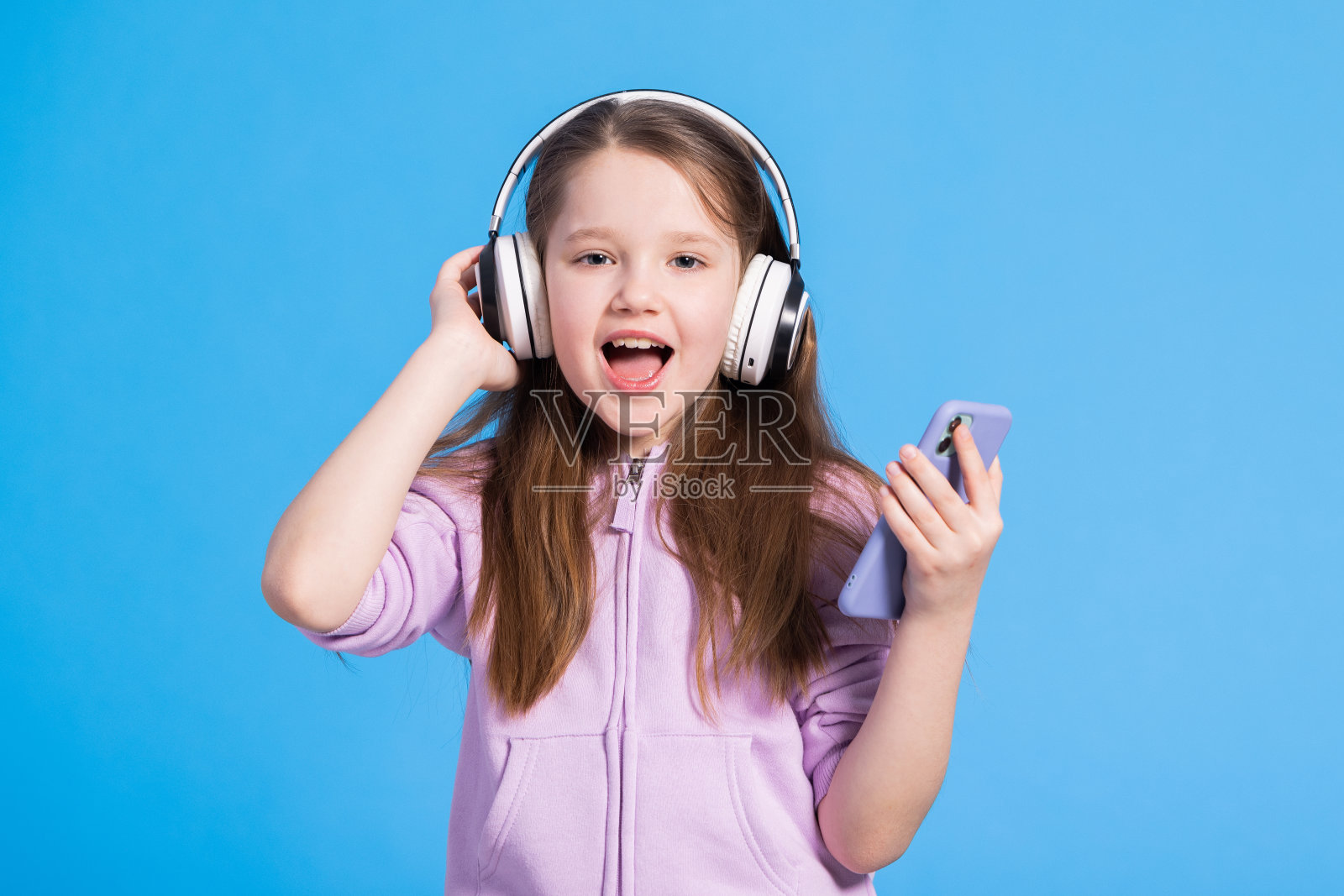 女孩可爱的小孩戴着耳机听音乐。蓝色背景。你最喜欢的歌手唱的歌。最好的免费音乐应用程序为您的移动设备。喜欢的声音照片摄影图片