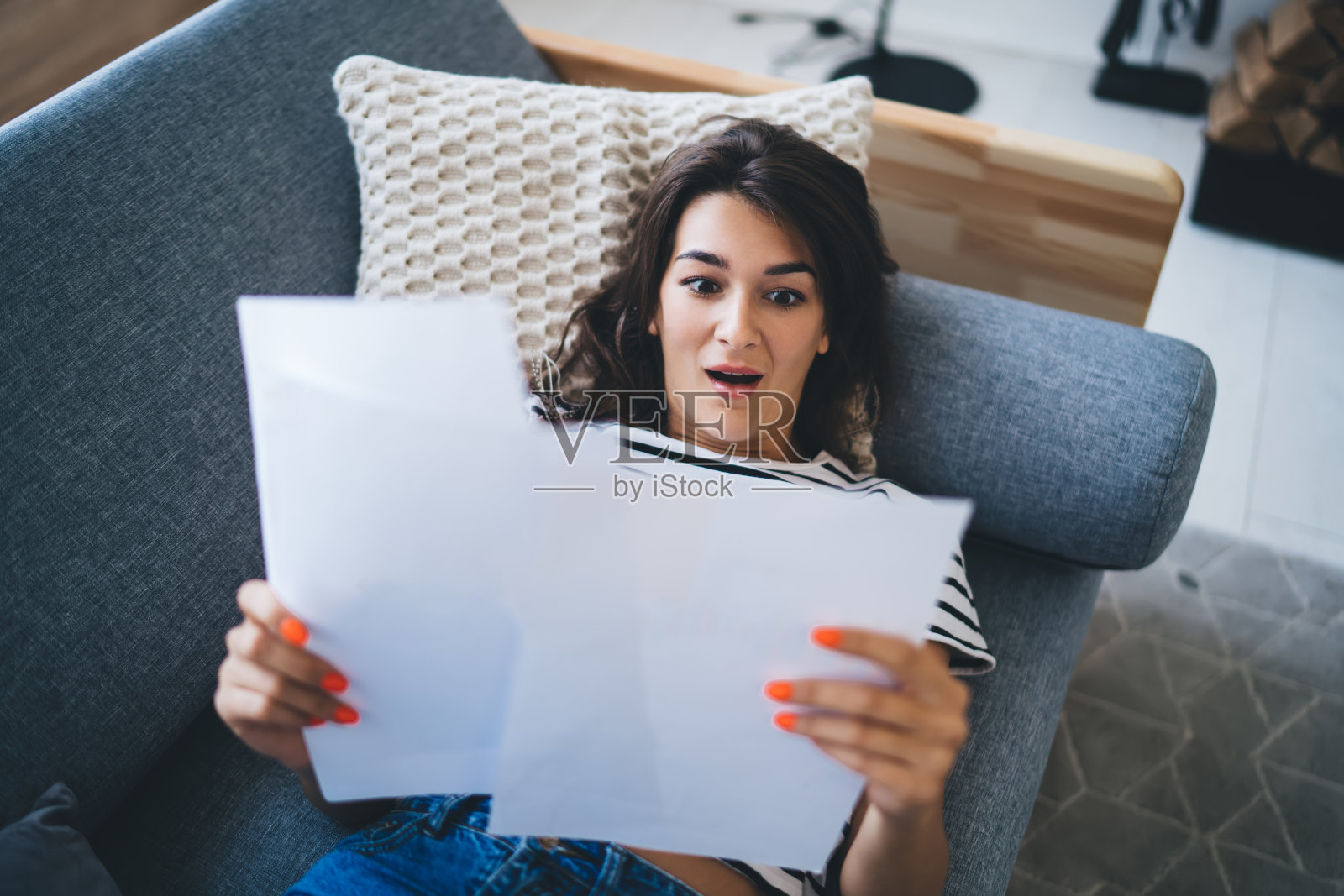 惊讶的女人躺在沙发上看文件照片摄影图片