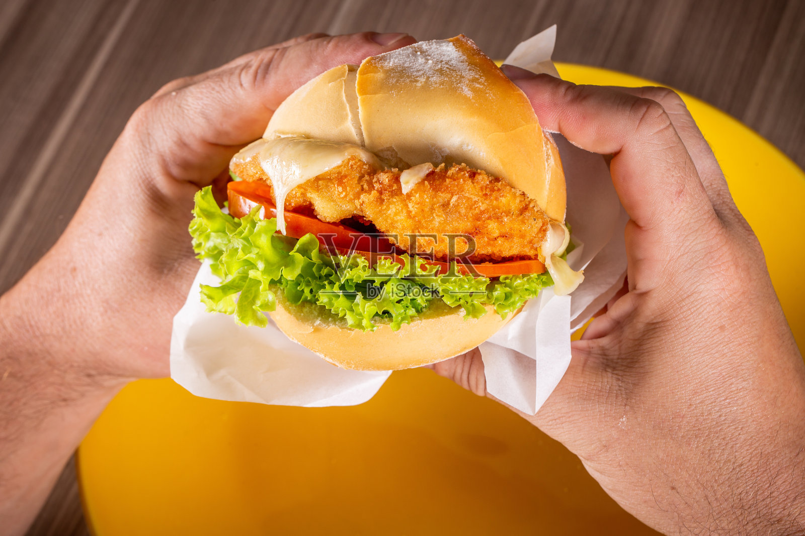 吃炸鸡汉堡加奶酪、生菜和番茄的人照片摄影图片