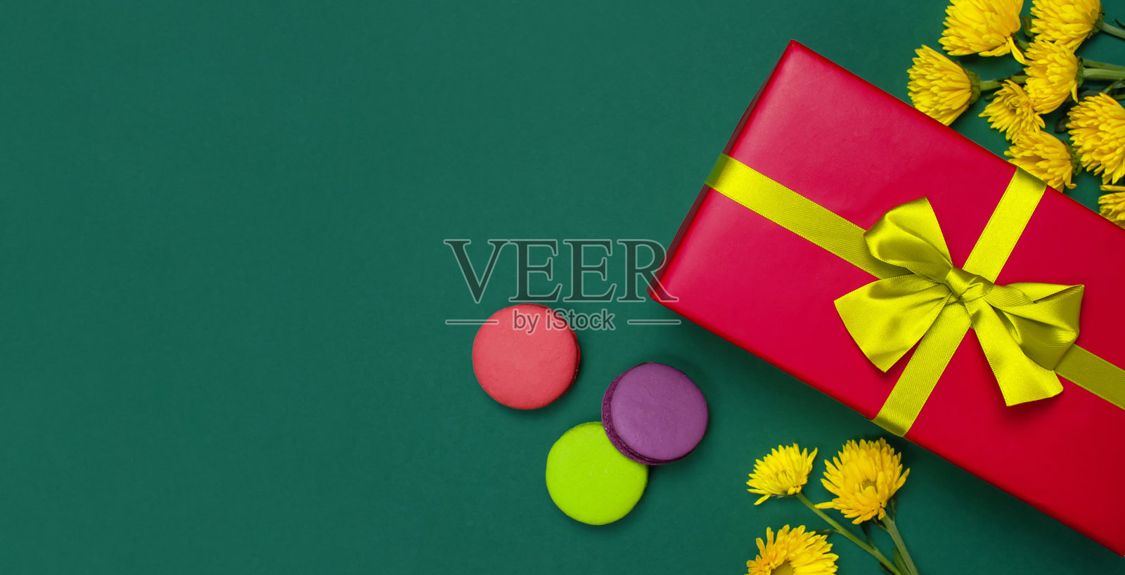红色礼盒与金色丝带黄色菊花蛋糕马卡龙马卡龙在深绿色背景俯视图平躺。节日概念，生日礼物，情人节或周年纪念。恭喜后台复制空间。照片摄影图片