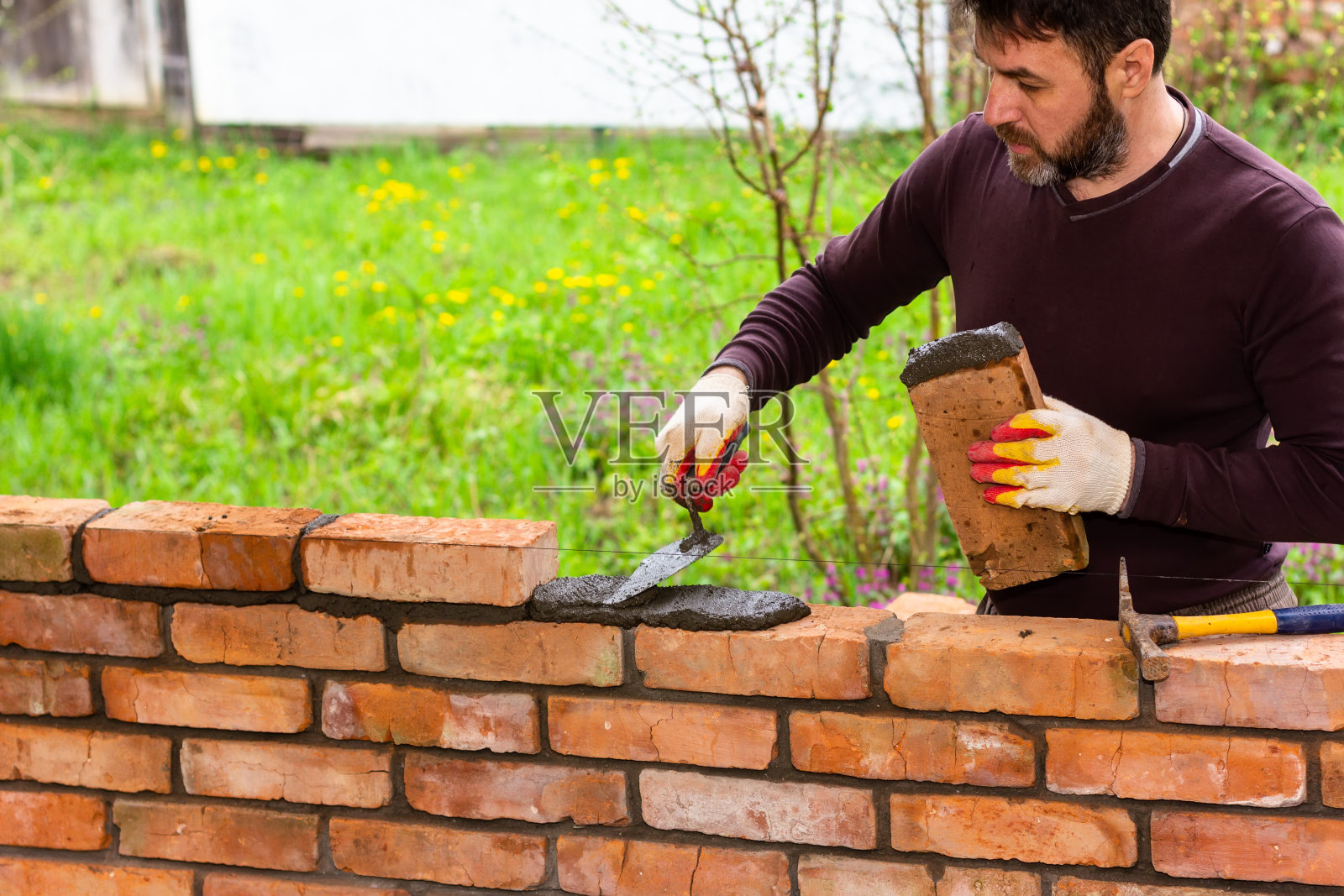 一个人用砖头砌了一堵墙，把一块砖头放在水泥沙砂浆上照片摄影图片