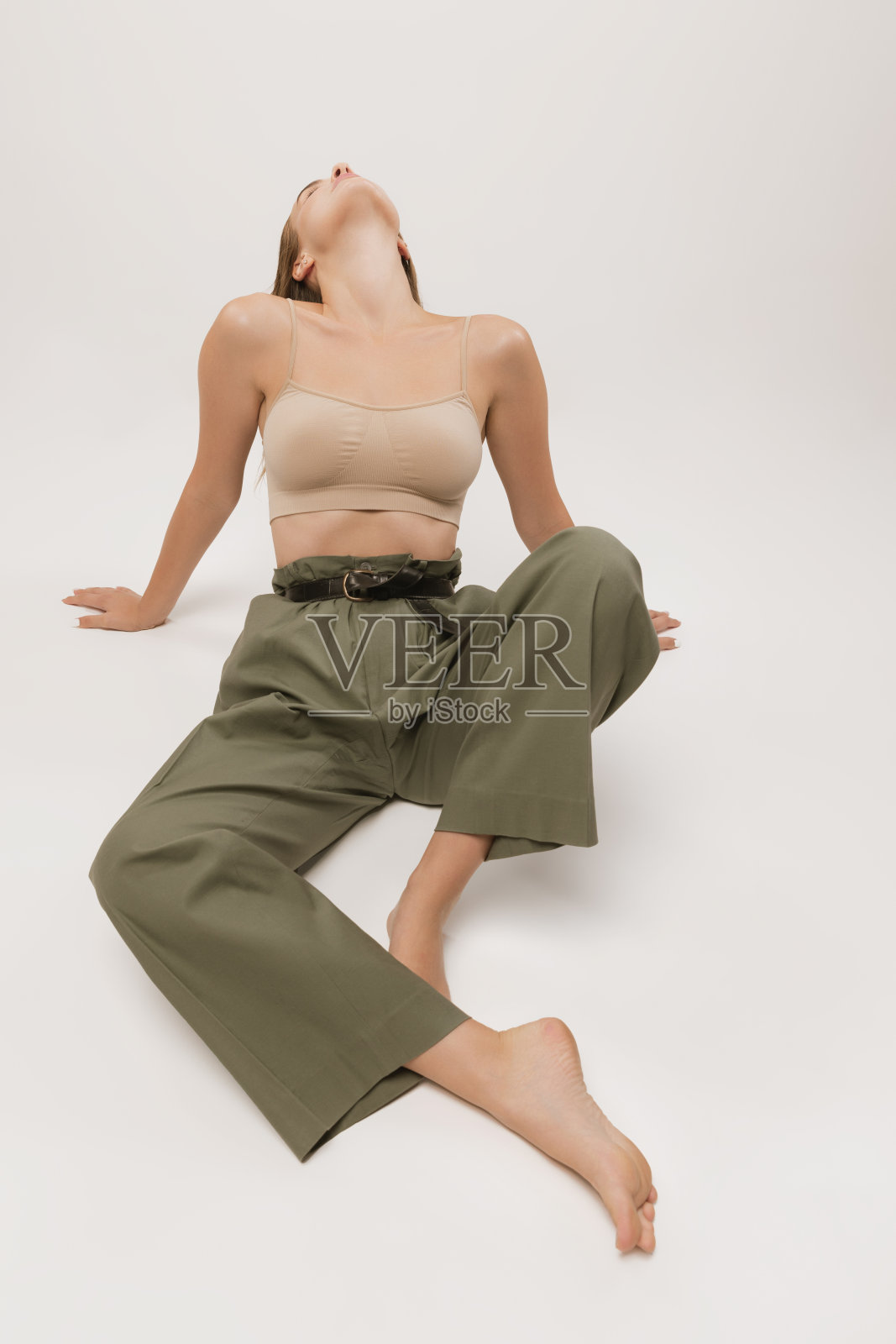 工作室拍摄的漂亮的年轻女孩长卷头发和自然的化妆，穿着露脐上衣和休闲裤子摆姿势在白色背景。照片摄影图片